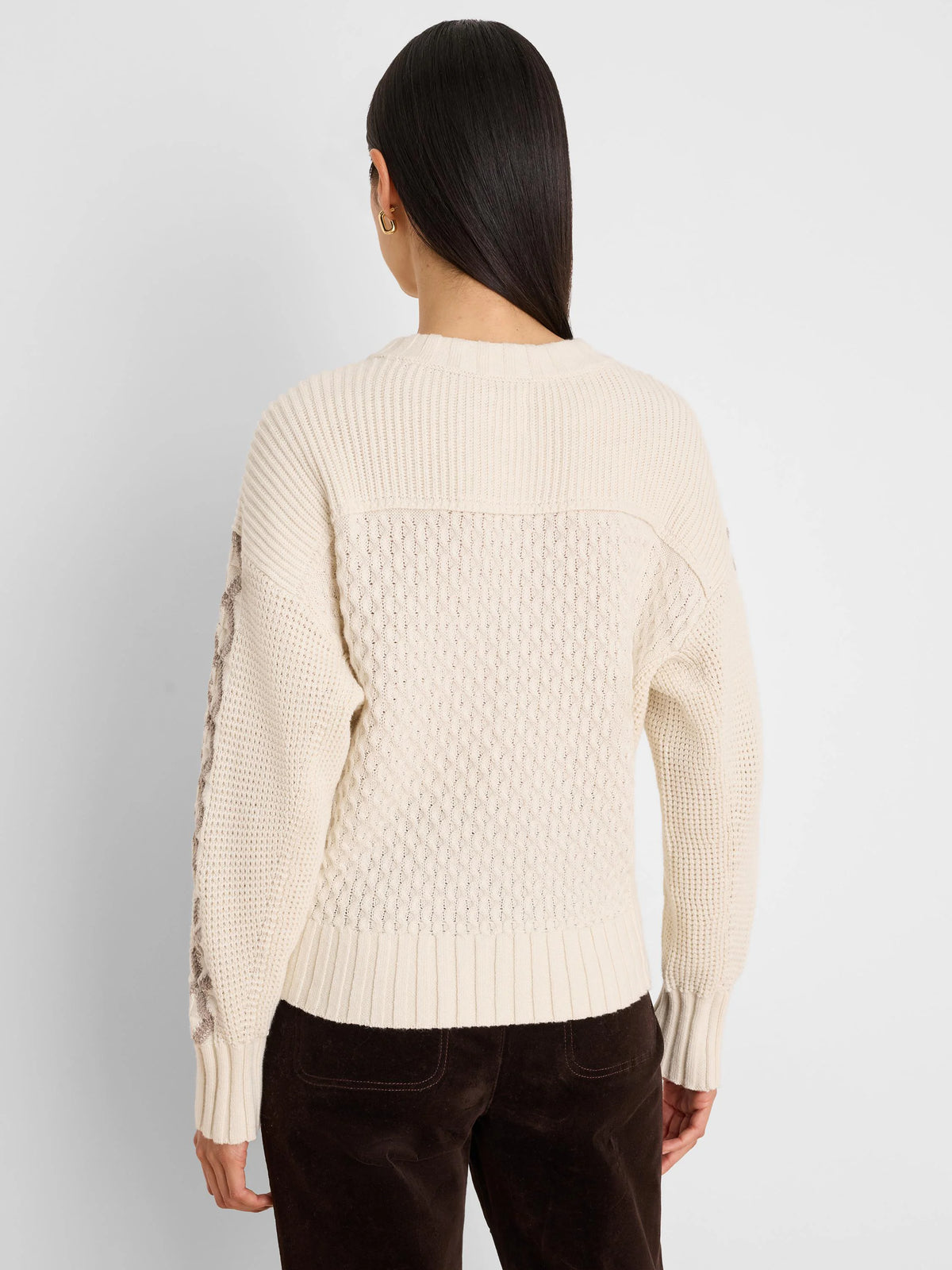 Cream cable knit sweater, back view. Tan criss-cross pattern on outer sleeves. Ribbed neck, cuffs, and hem.