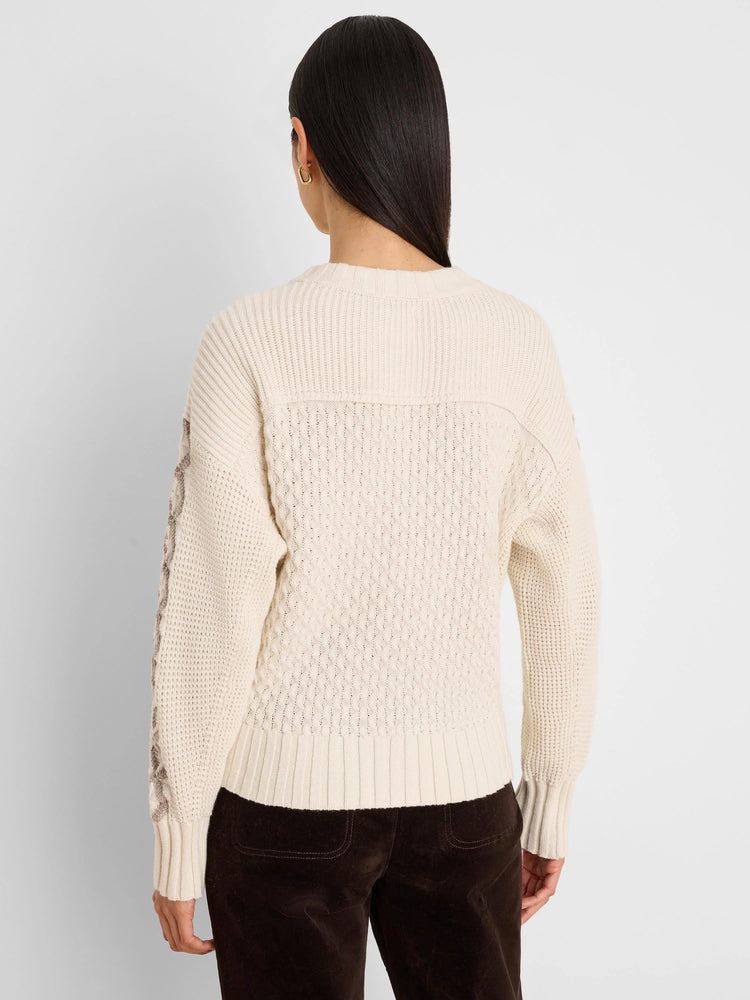 Cream cable knit sweater, back view. Tan criss-cross pattern on outer sleeves. Ribbed neck, cuffs, and hem.