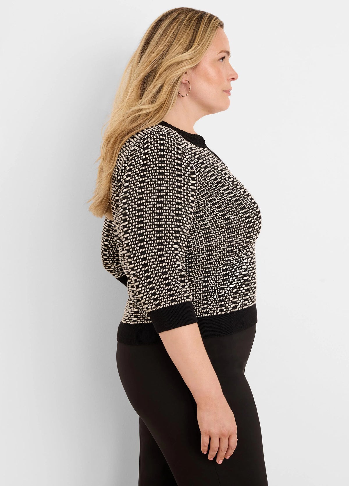 A woman wears a black and cream geometric knit sweater with lace trim at the neckline and 3/4 sleeves.