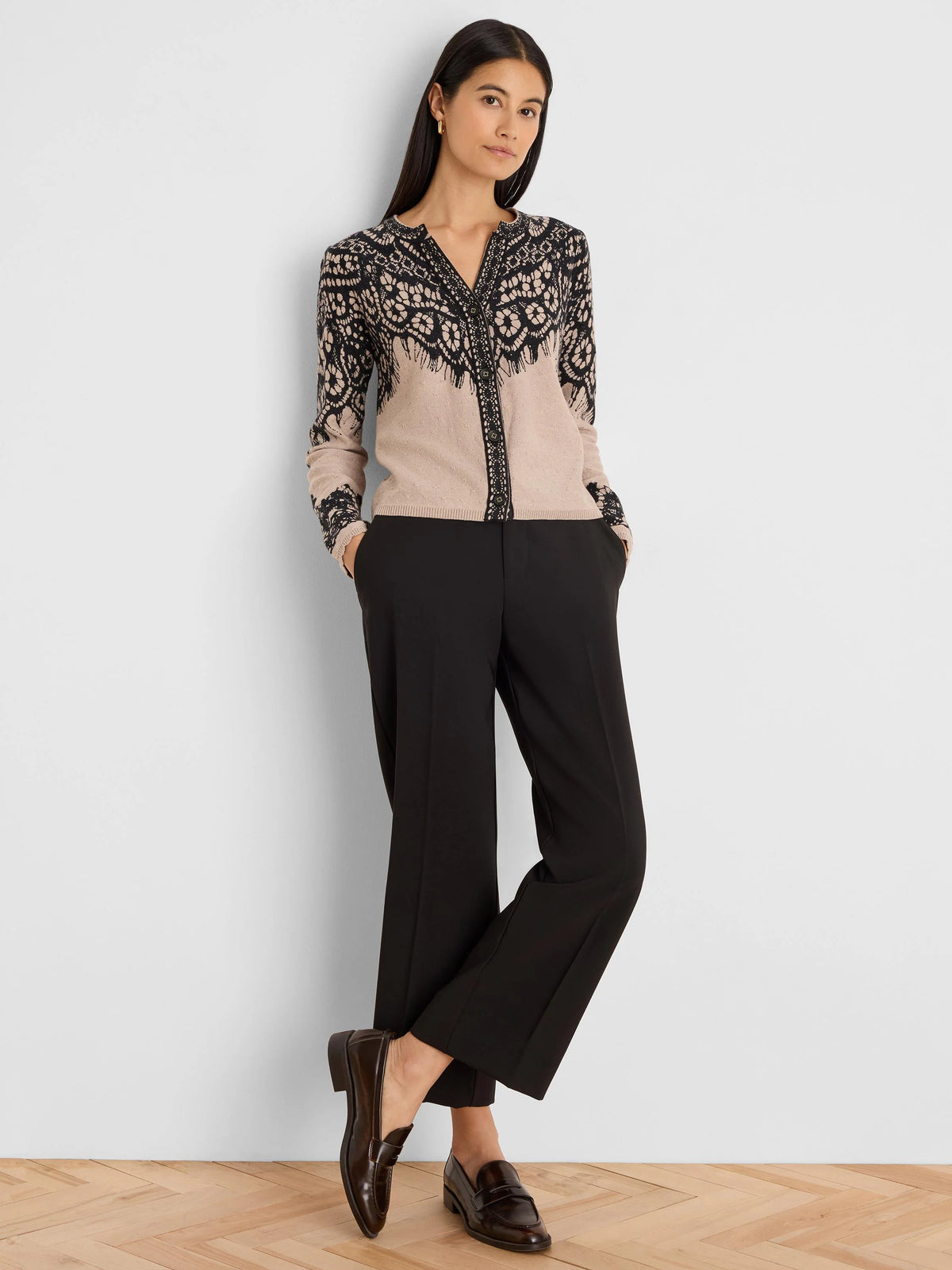 Beige cardigan with intricate black lace print. Features a button-front closure and a rounded neckline.