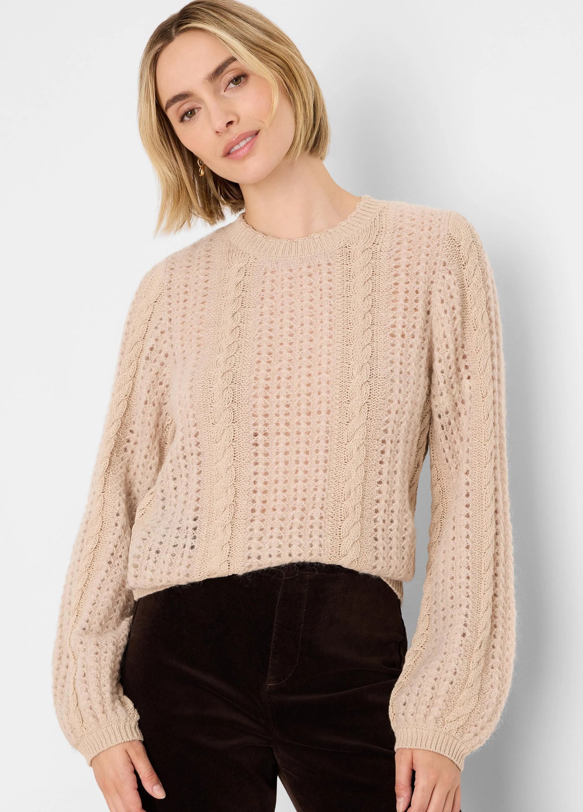 Beige open-knit sweater with fuzzy texture, prominent cable-knit panels, and puffed long sleeves.