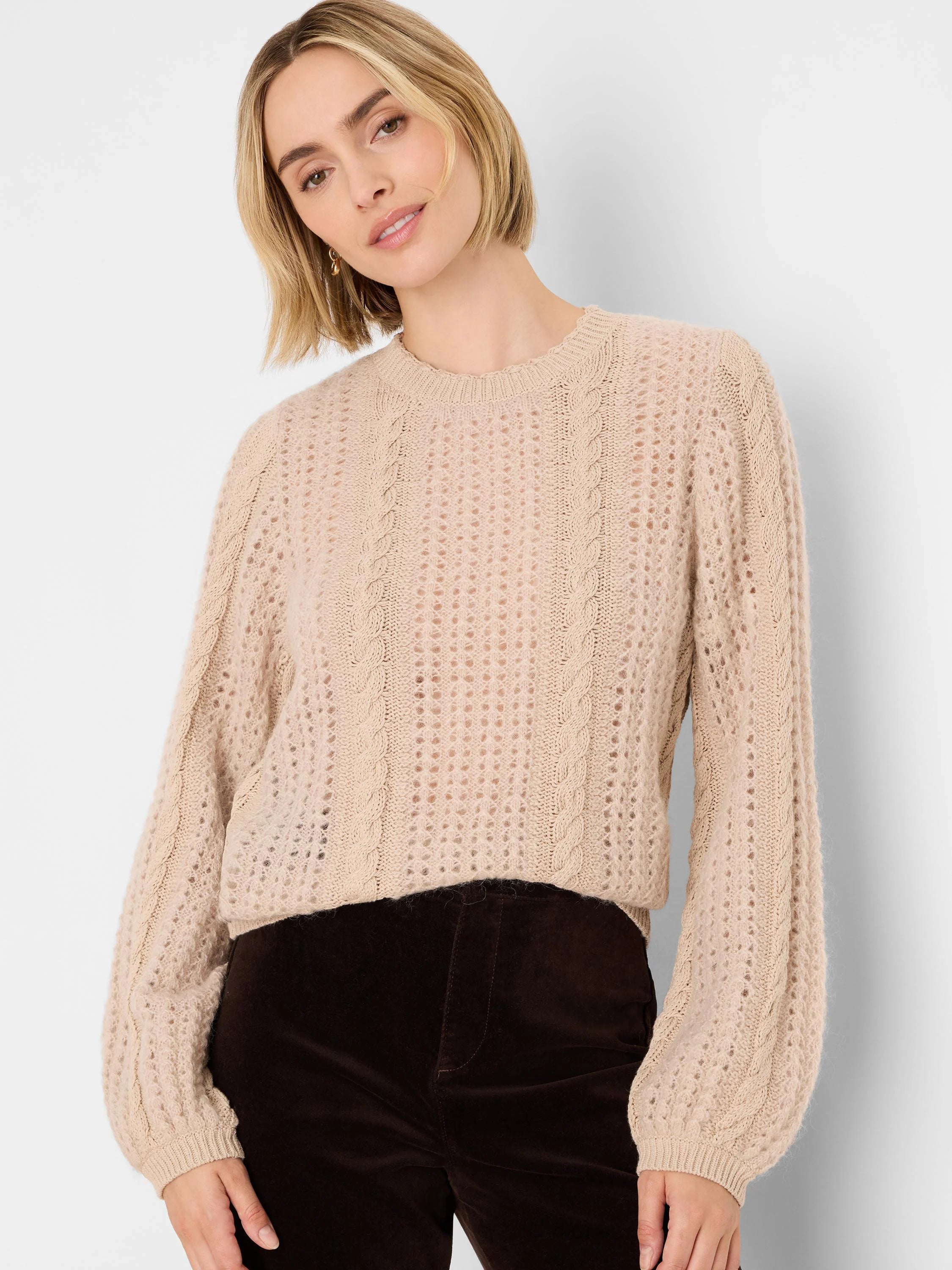 Beige open-knit sweater with fuzzy texture, prominent cable-knit panels, and puffed long sleeves.