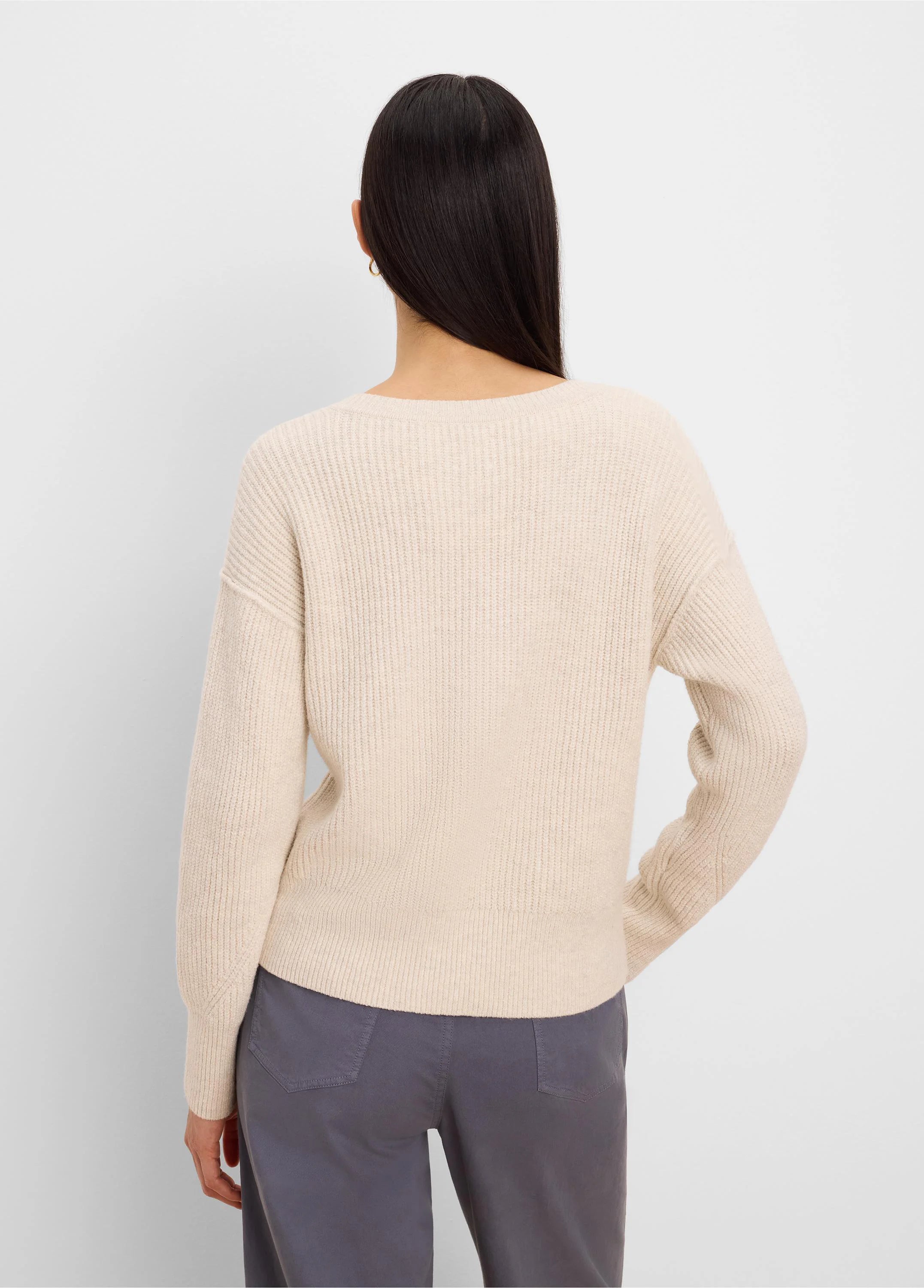 Light beige ribbed knit pullover sweater, shown from the back on a model. Features long sleeves and a relaxed fit.
