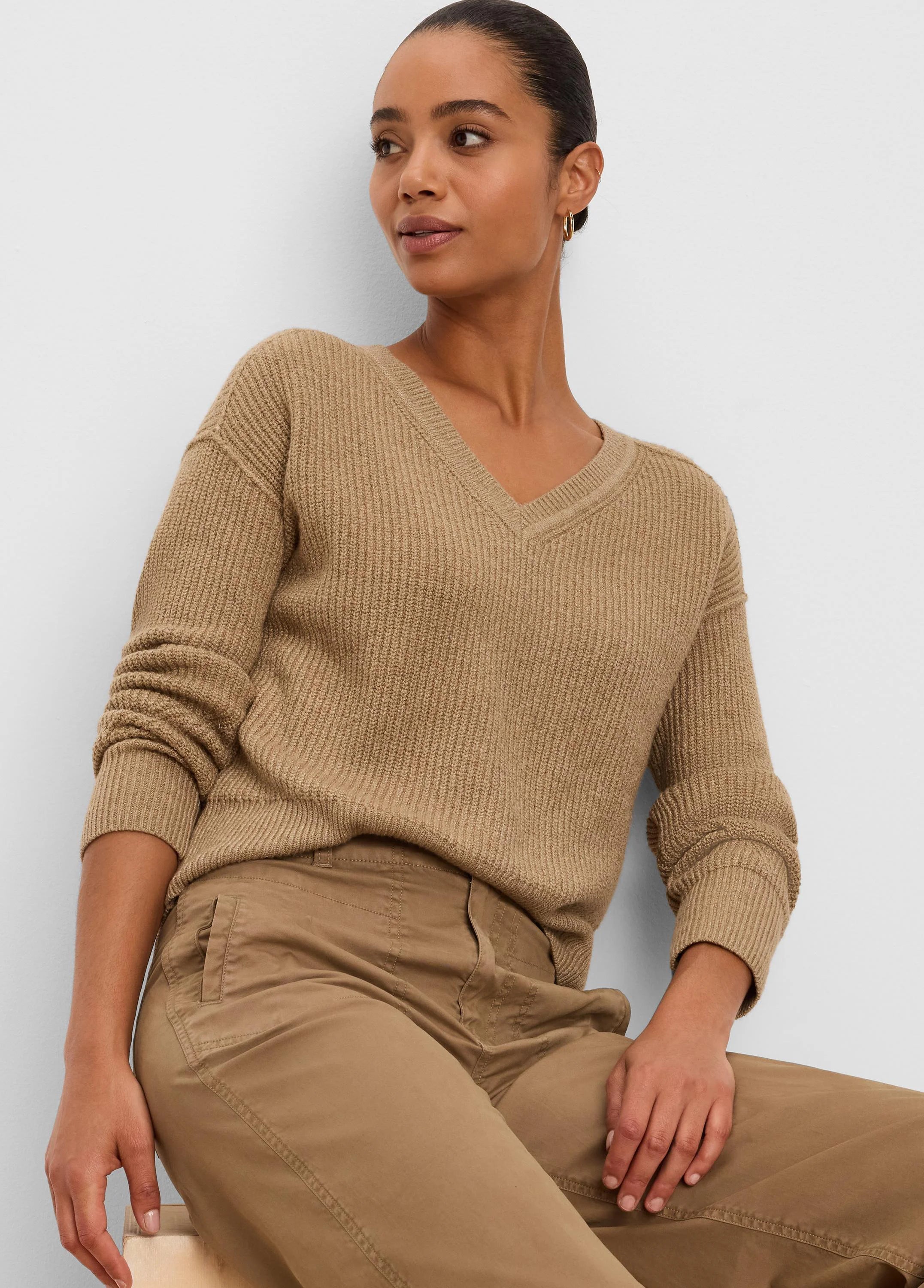 Model wearing a camel V-neck sweater with a distinct vertical ribbed knit pattern and ribbed cuffs.