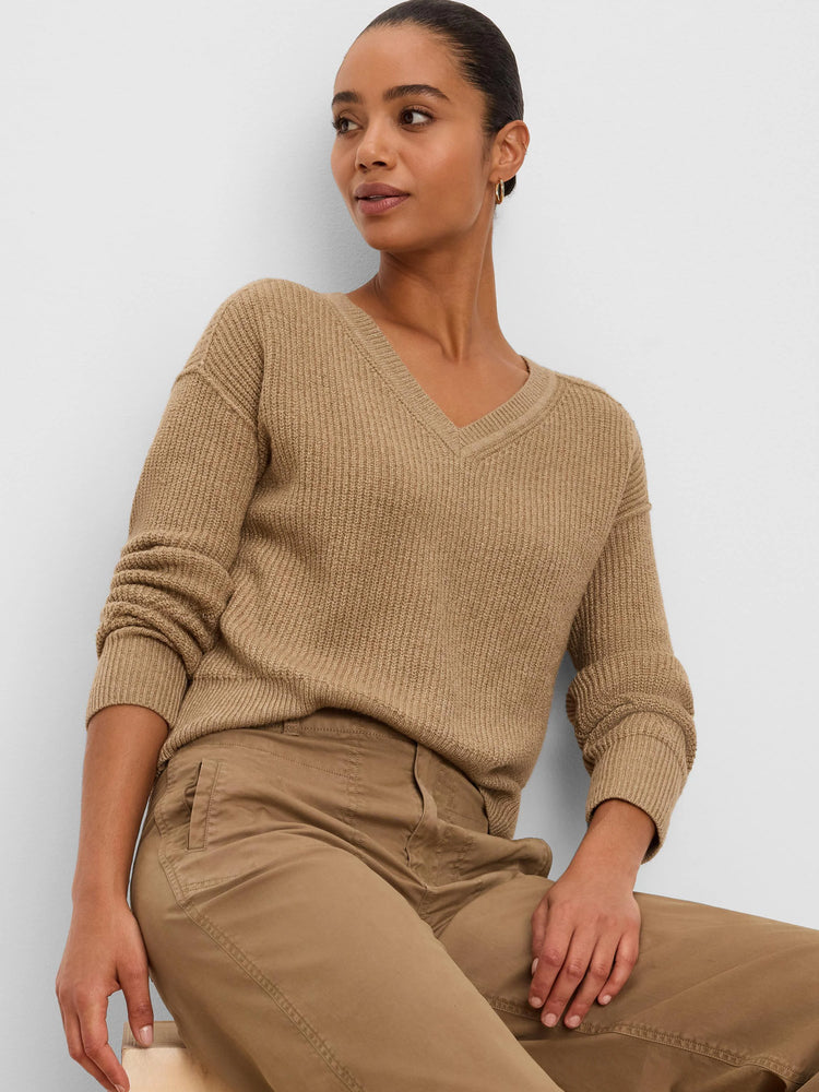 Model wearing a camel V-neck sweater with a distinct vertical ribbed knit pattern and ribbed cuffs.