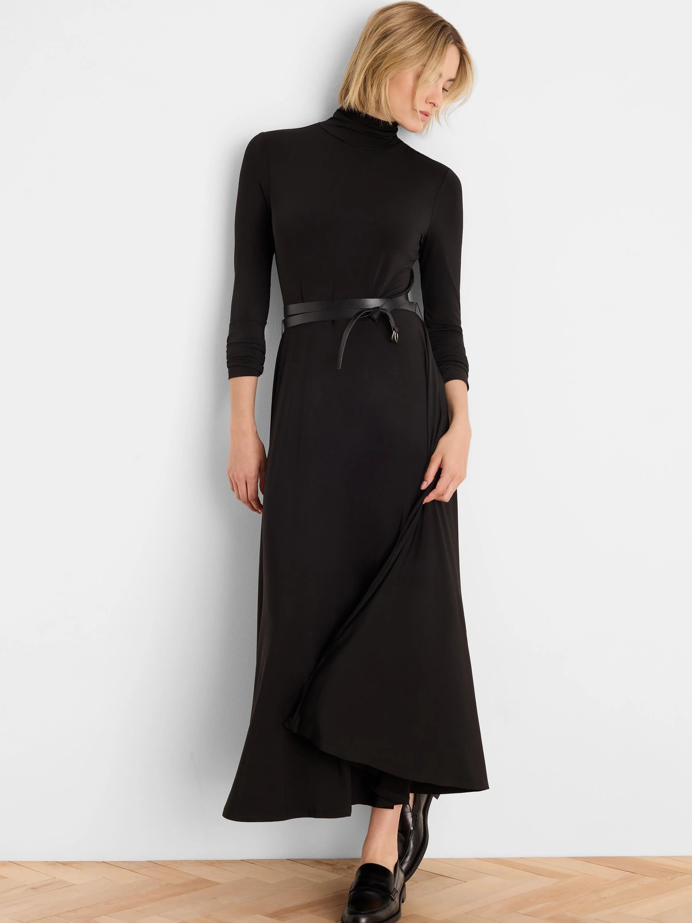 Black high neck maxi dress with 3/4 sleeves and a thin black tie belt. Skirt features a diagonal front drape.