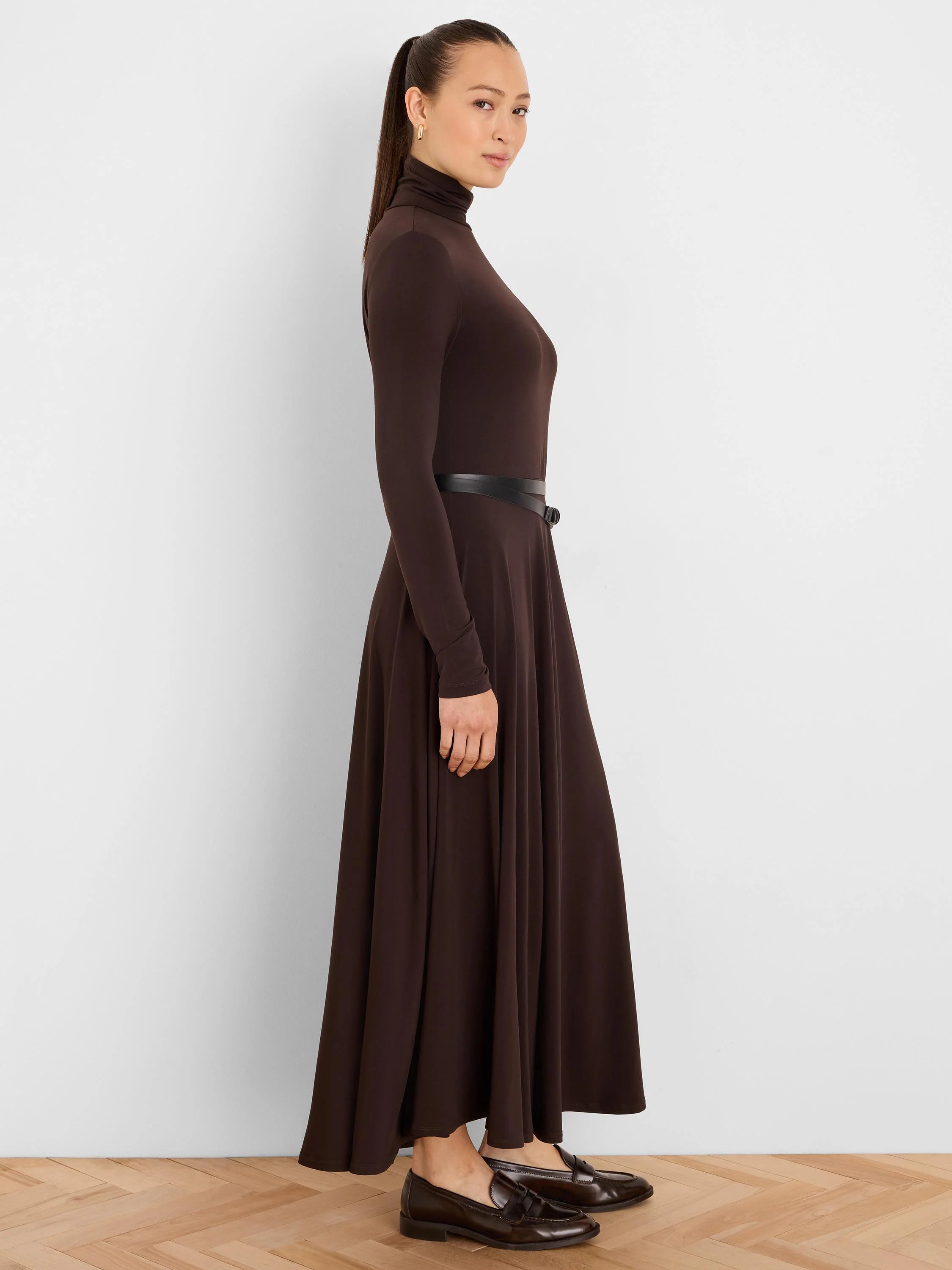 Brown high-neck dress with long sleeves, flared maxi skirt, and a thin black belt at the waist.