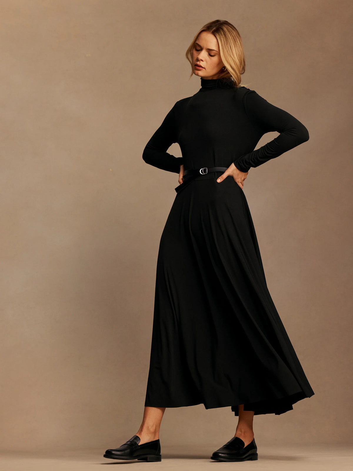 Black high neck maxi dress with long sleeves and a flowy skirt, worn by a model with a belt.