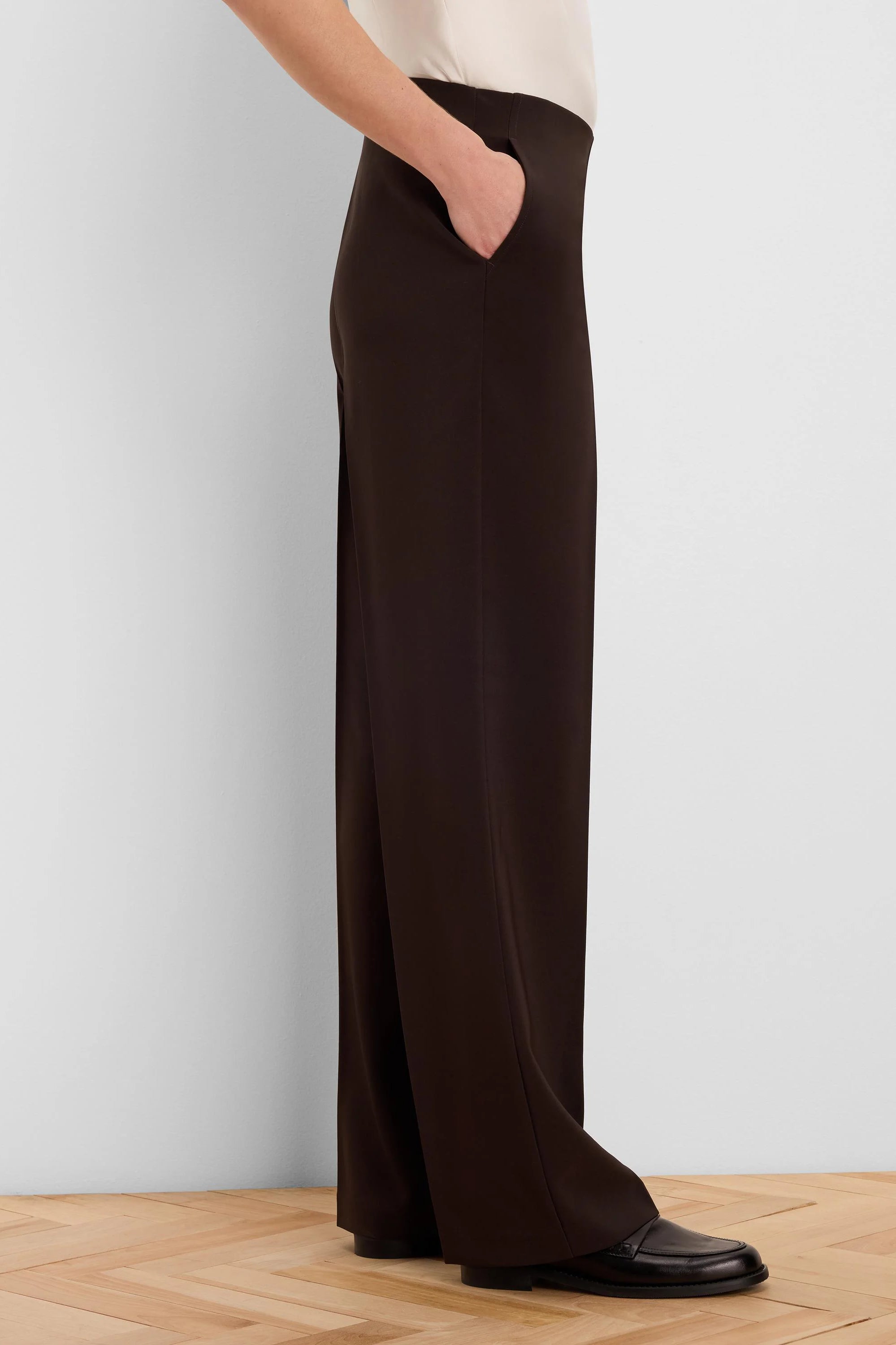 Dark brown wide-leg pants with a sleek finish, featuring a side slash pocket with a hand in it. Paired with a cream top.