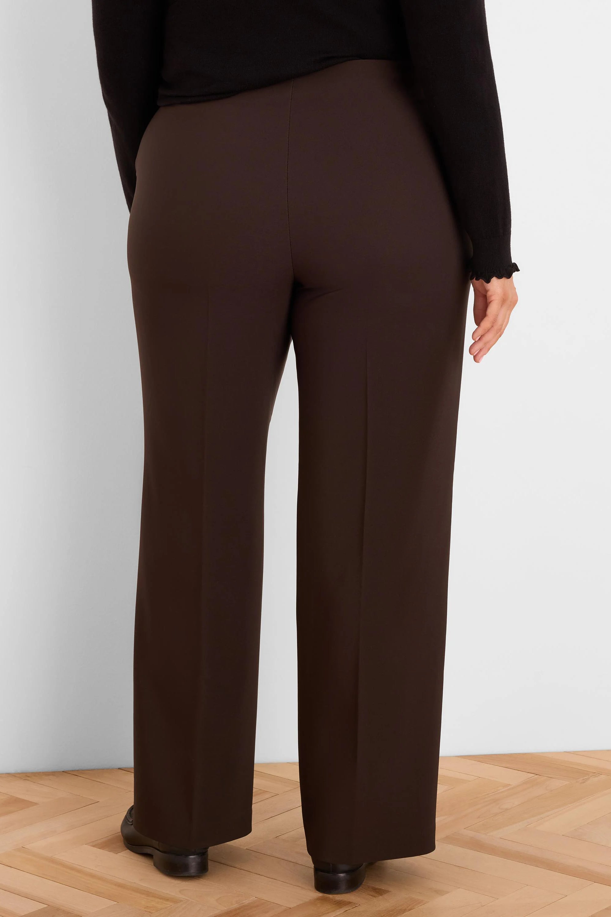 Deep brown wide-leg pants with sharp vertical leg creases, shown on a model from behind.