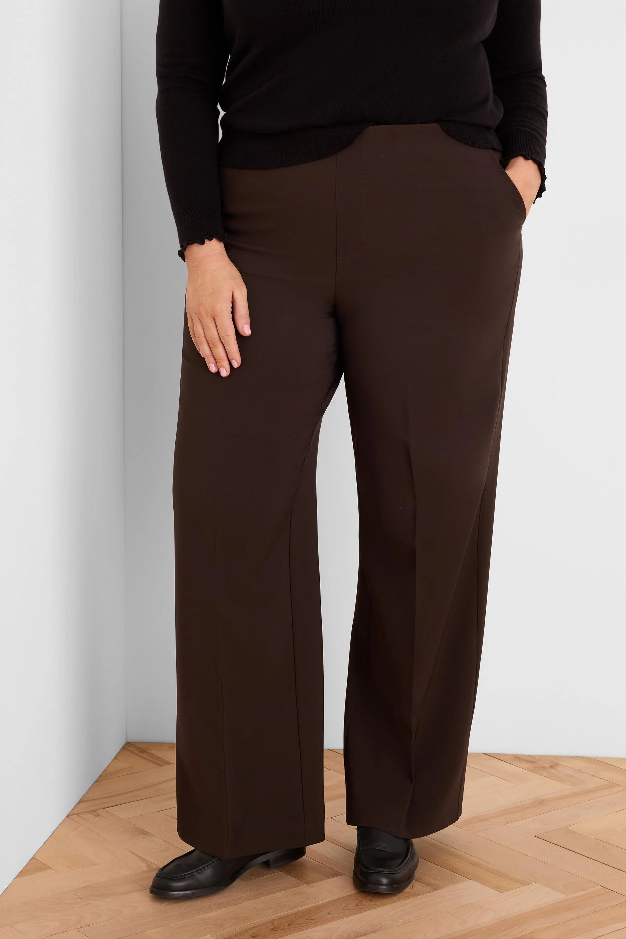 Dark brown wide-leg pants. Smooth fabric, full length, with a hand in one pocket.