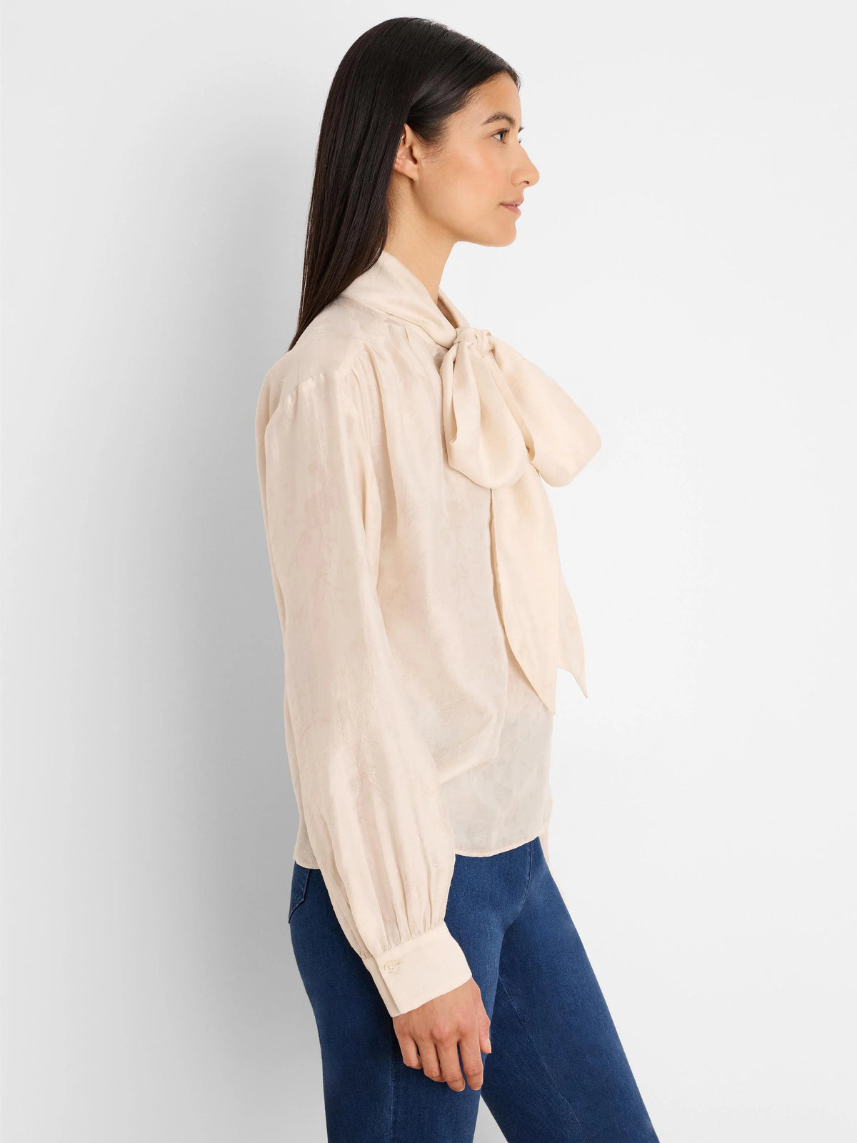 Cream crinkle-textured top with a large neck tie bow, long sleeves, and buttoned cuffs.