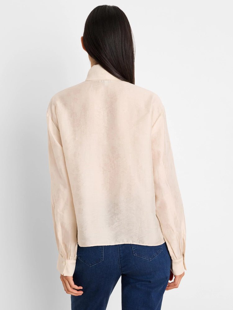 Pale peach crinkle top with subtle floral texture. Long sleeves, relaxed fit, shown from the back.
