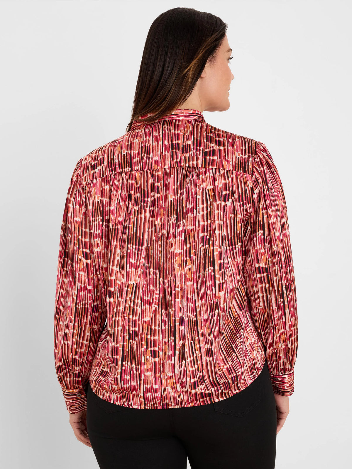 Back view: Shirt with red, orange, black abstract vertical pattern and extensive pleating. Long sleeves.