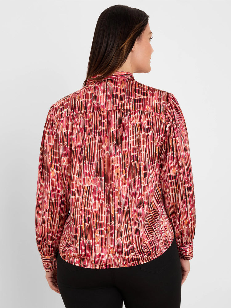 Back view: Shirt with red, orange, black abstract vertical pattern and extensive pleating. Long sleeves.