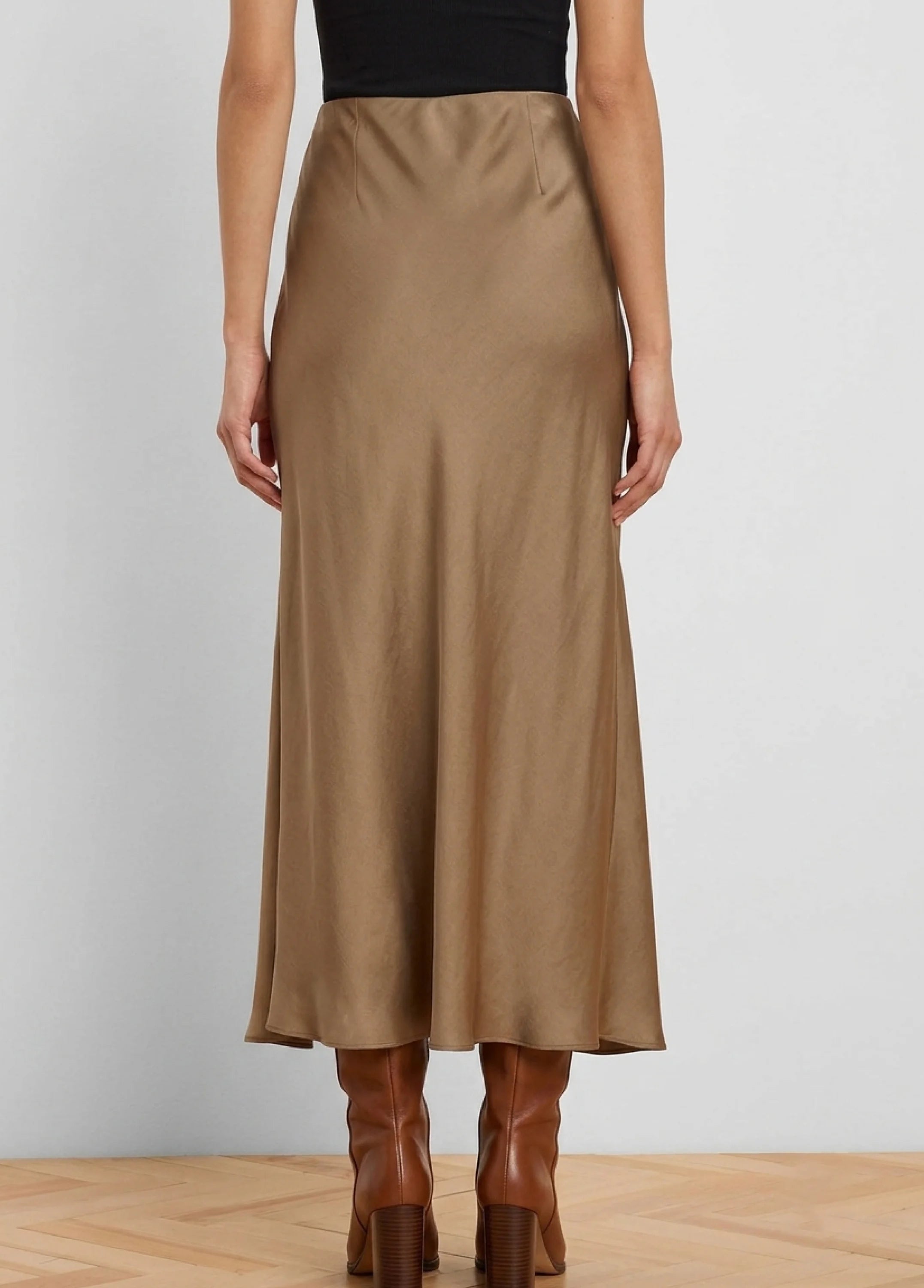 Back view of a light brown, glossy slip skirt. It's midi length with a subtle sheen, worn with a black top and brown boots.