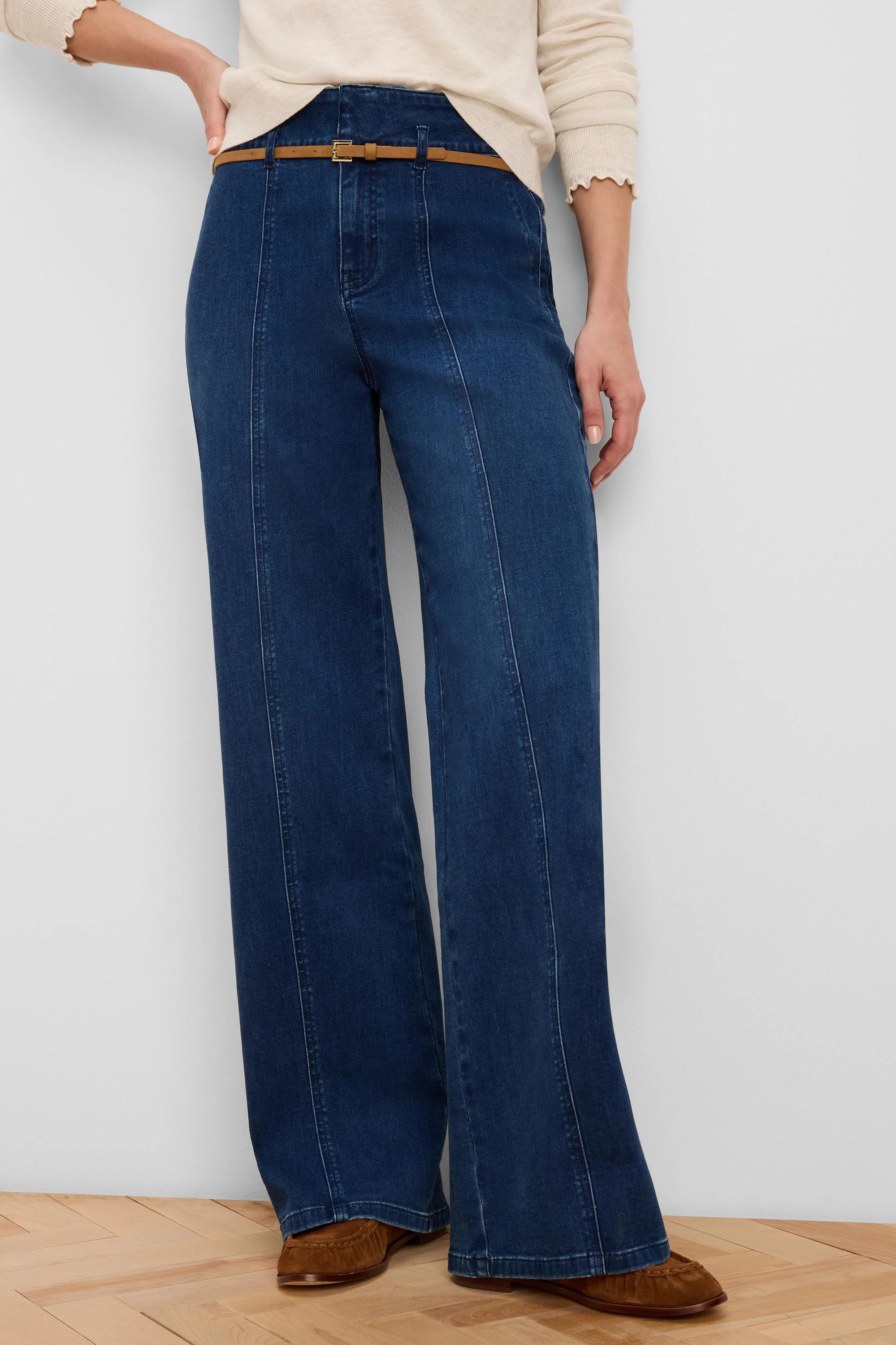 Deep blue wide-leg jeans with front seam details and a thin tan belt around the high waist.