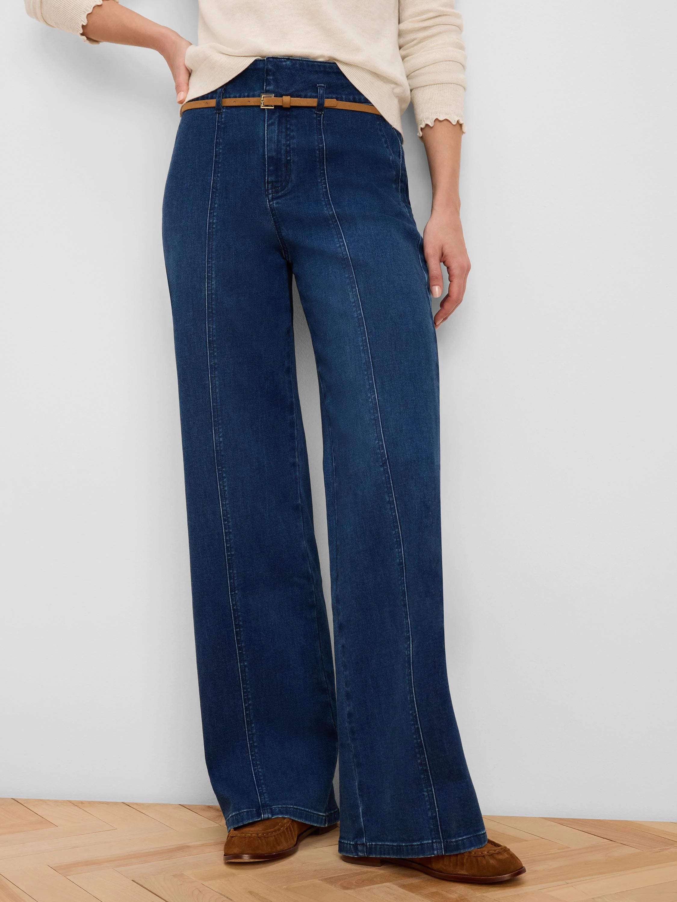 Deep blue wide-leg jeans with front seam details and a thin tan belt around the high waist.
