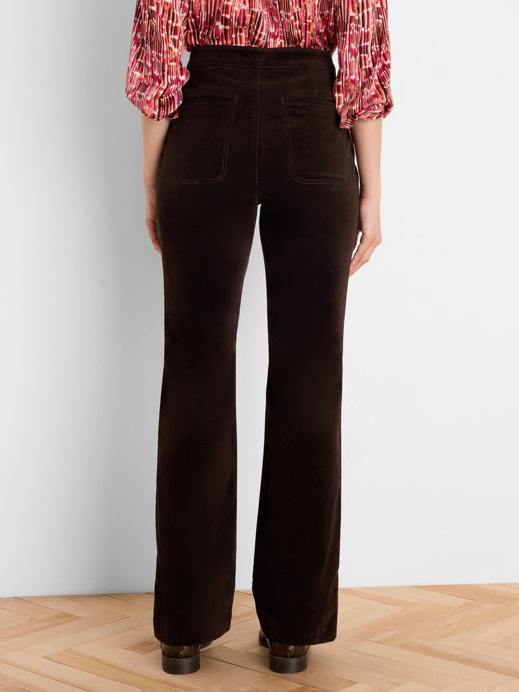 Dark brown velvet boot-cut pants on model from behind. Features back patch pockets and a subtle leg flare.