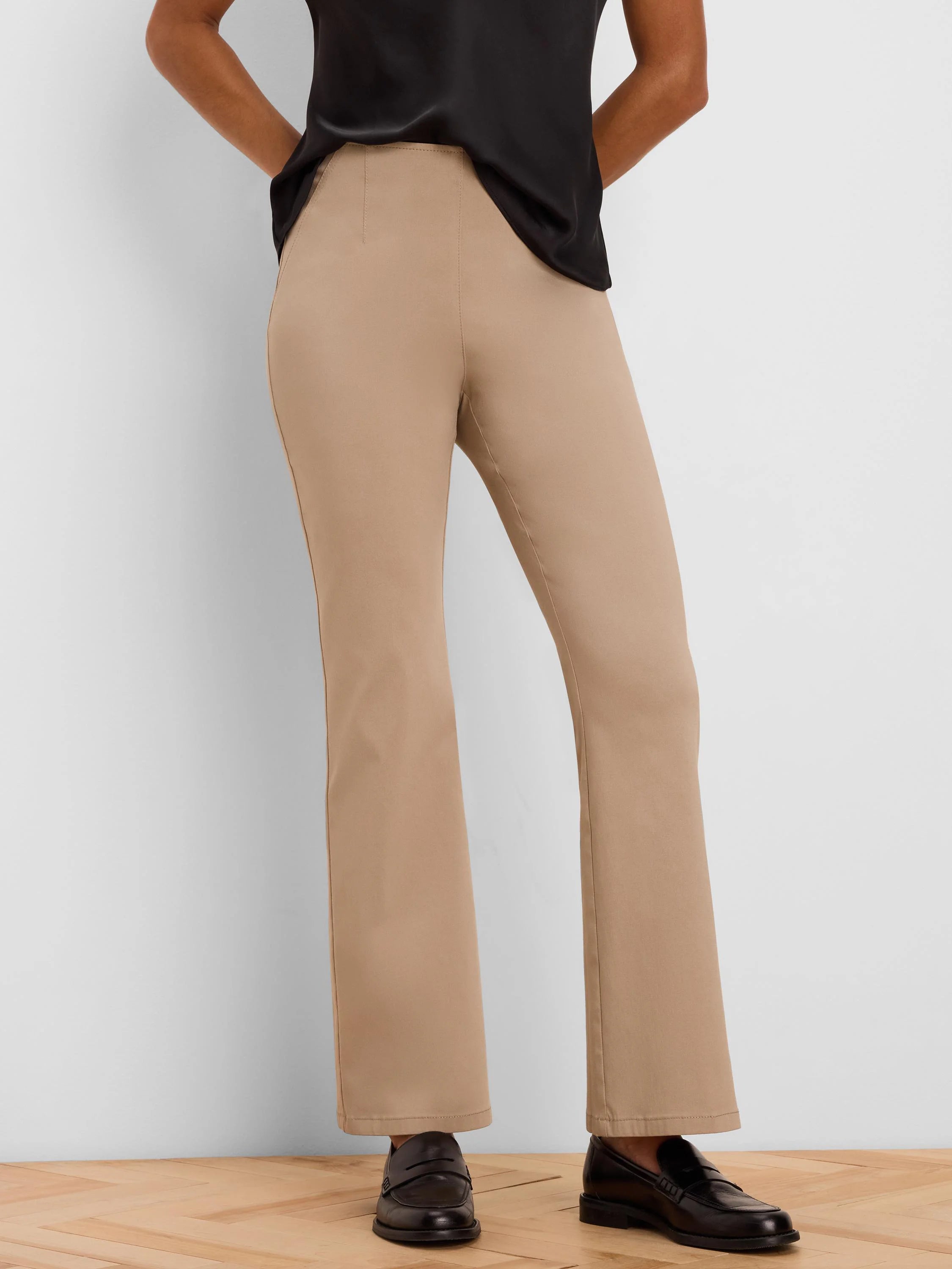Tan, high-waisted bootcut pants on a person. Slim-fit through legs, subtle flare at hem. Smooth fabric.