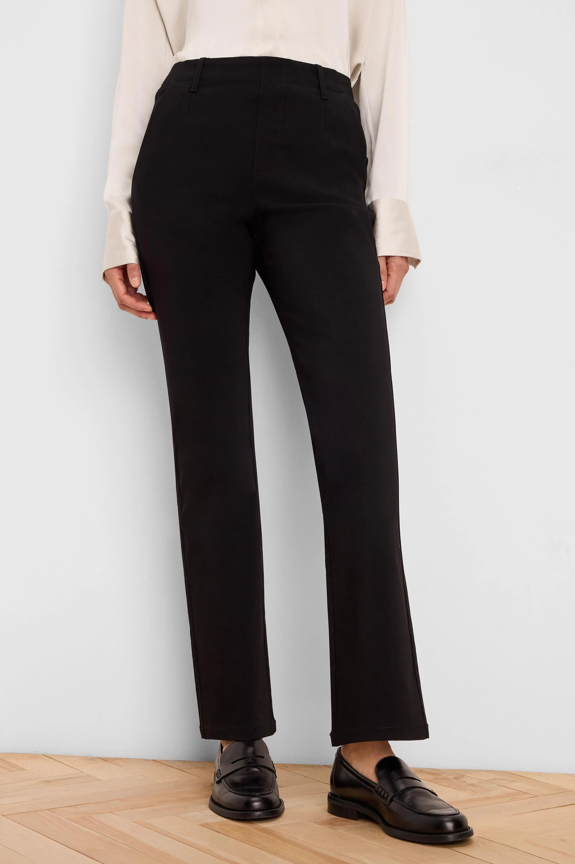 Black high-rise, straight-leg pants with a smooth finish, worn by a model with a light top and black loafers.