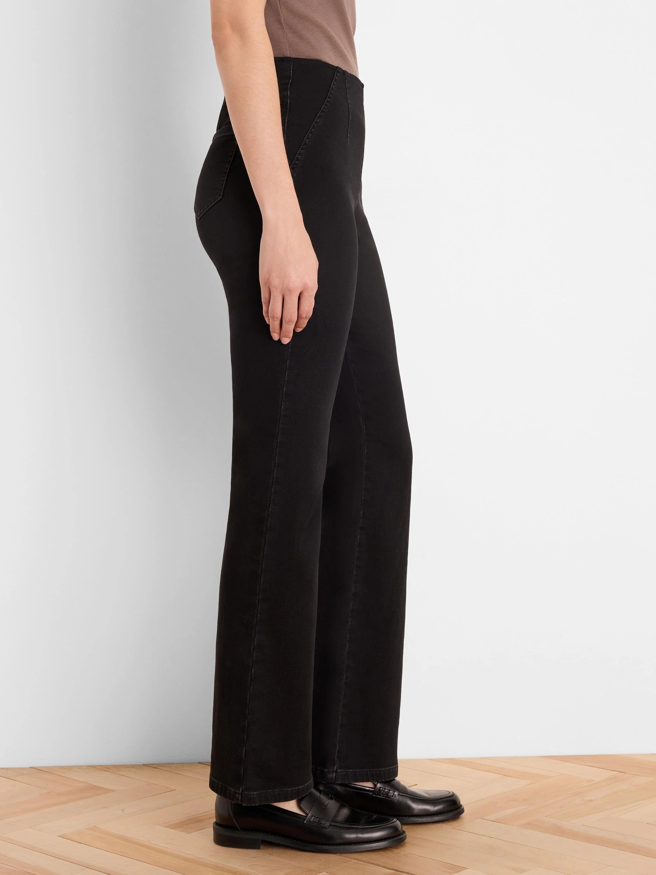 Black bootcut jeans, modeled from the side. They have a slight flare below the knee and subtle vertical seams.