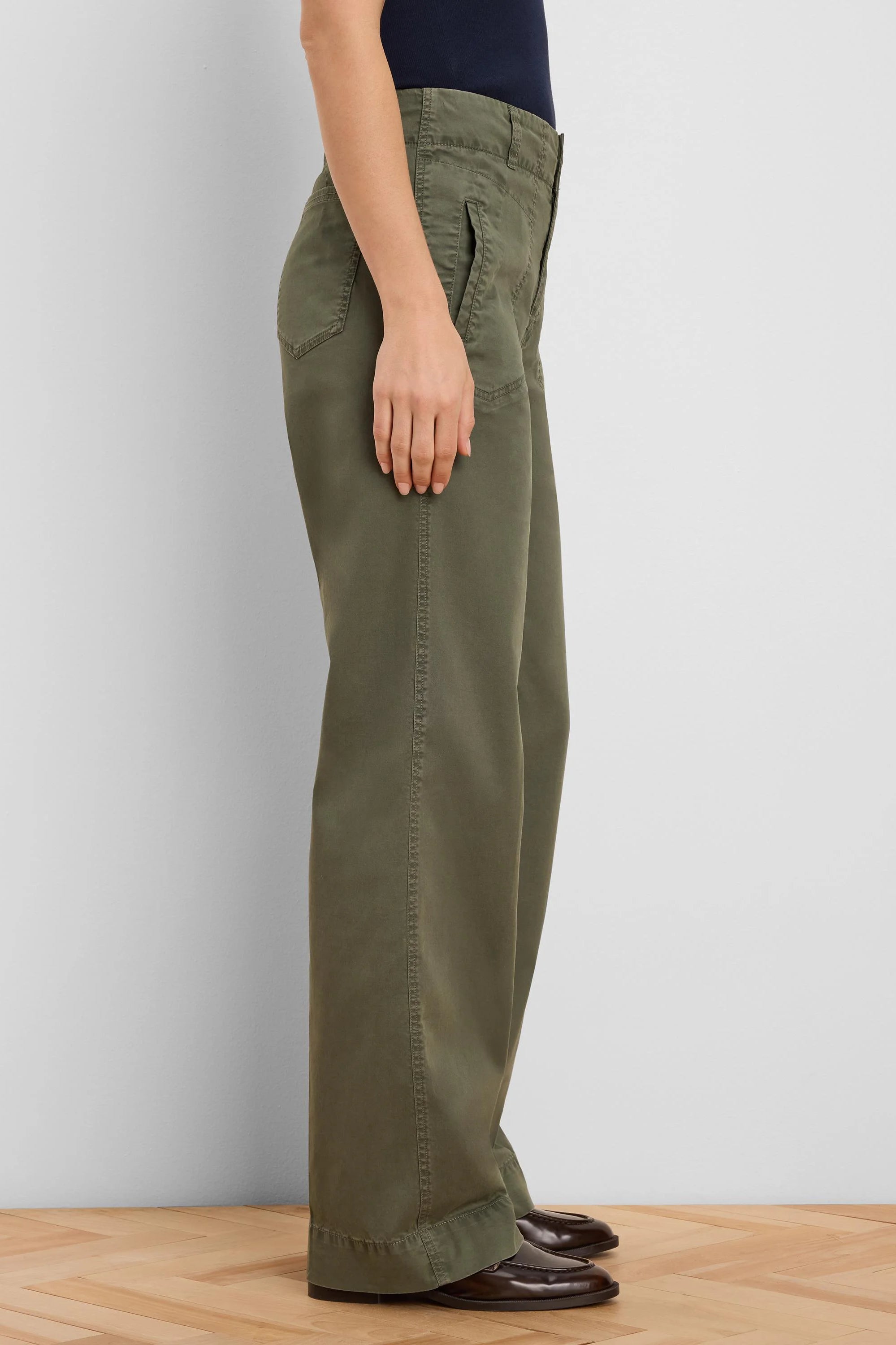 Olive green wide-leg pants with angled pockets and prominent outer leg stitching, shown on a person from the side.