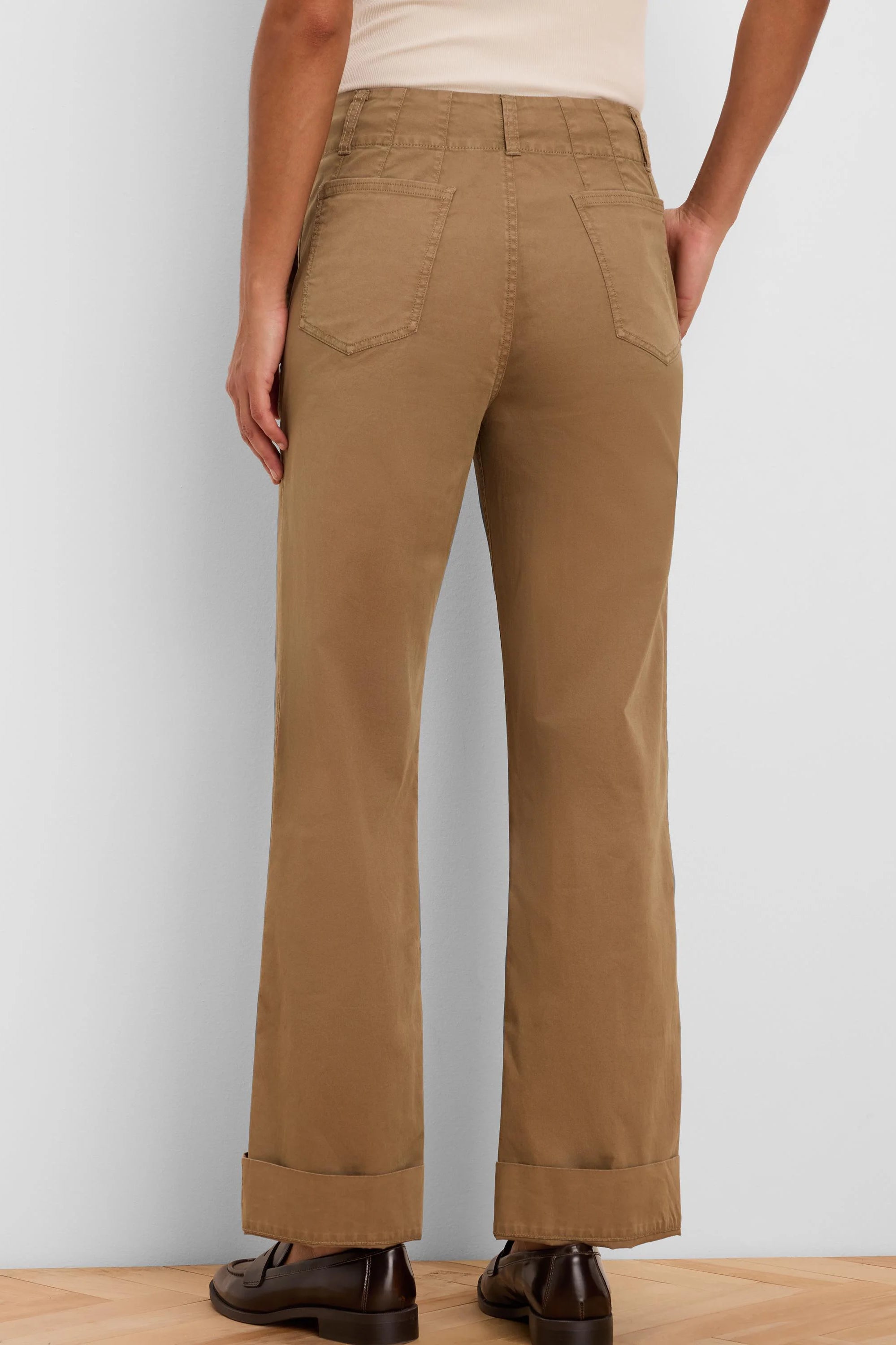 Tan high-waisted straight-leg pants, seen from behind, with patch back pockets and cuffed hems.