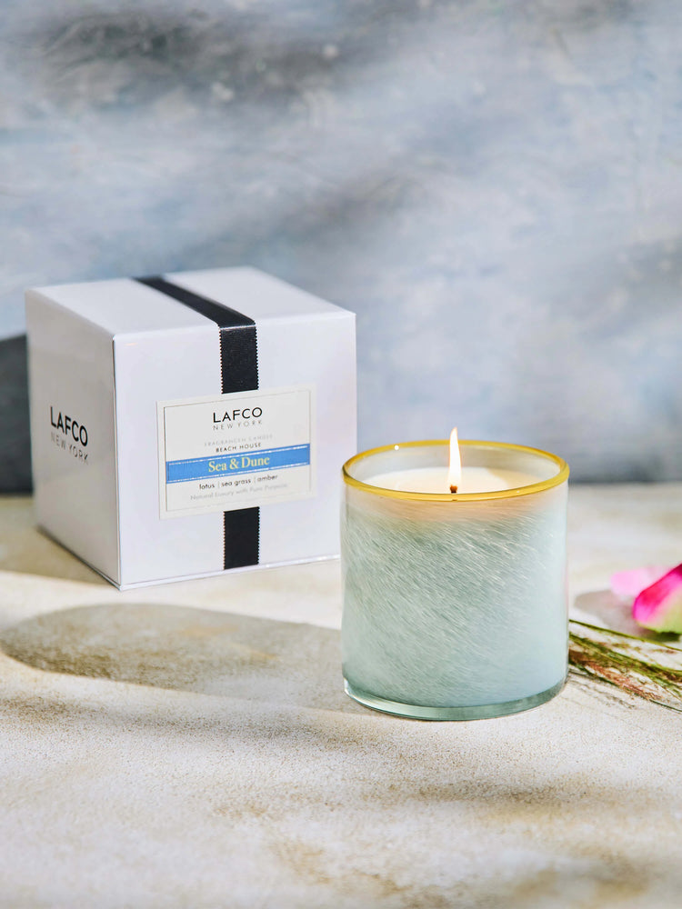 Lit candle in swirled light blue-green glass with gold rim. White box with black ribbon and blue-white label.
