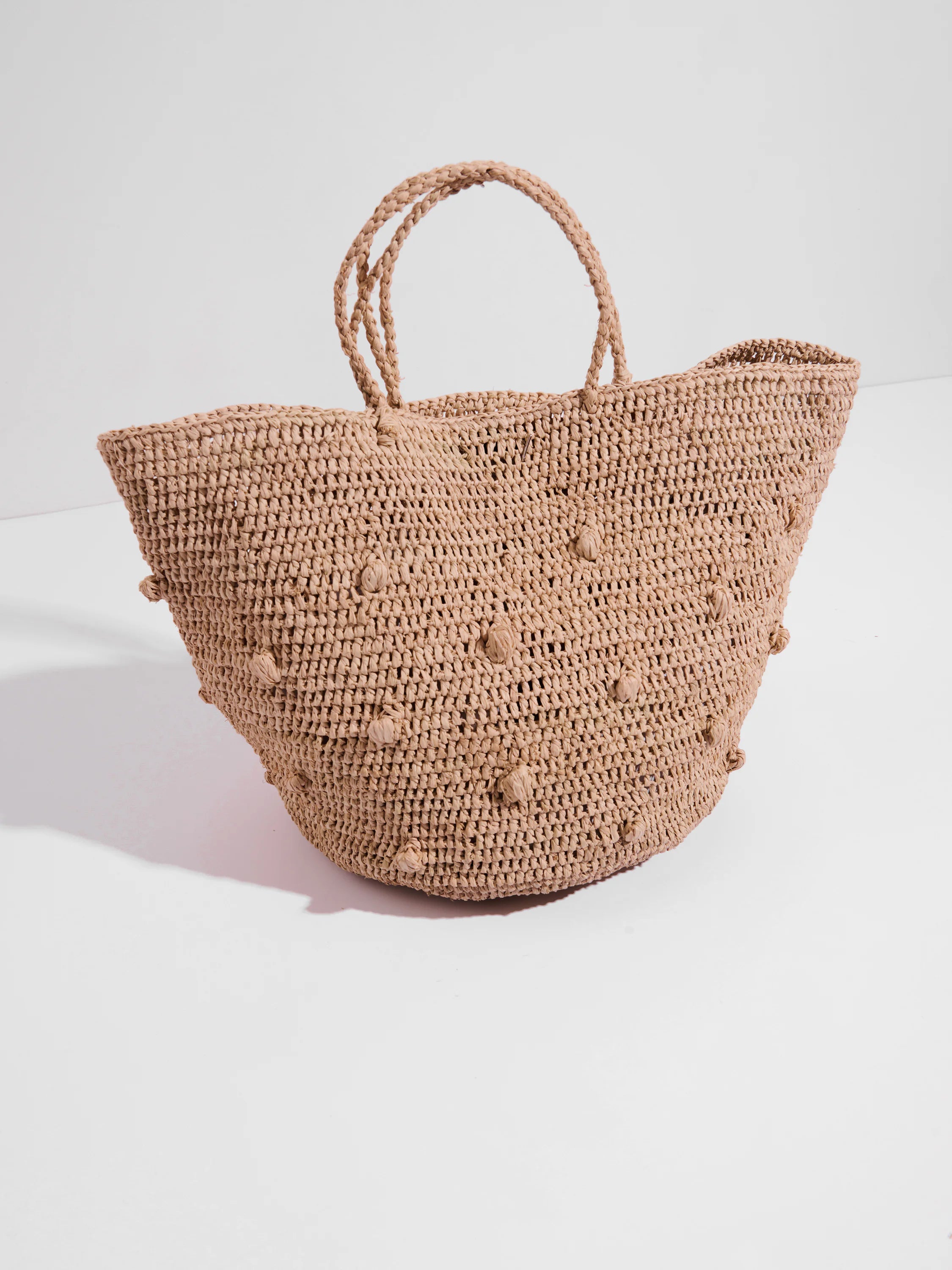 Beige crocheted tote bag with textured, small pom-pom accents. Double top handles.