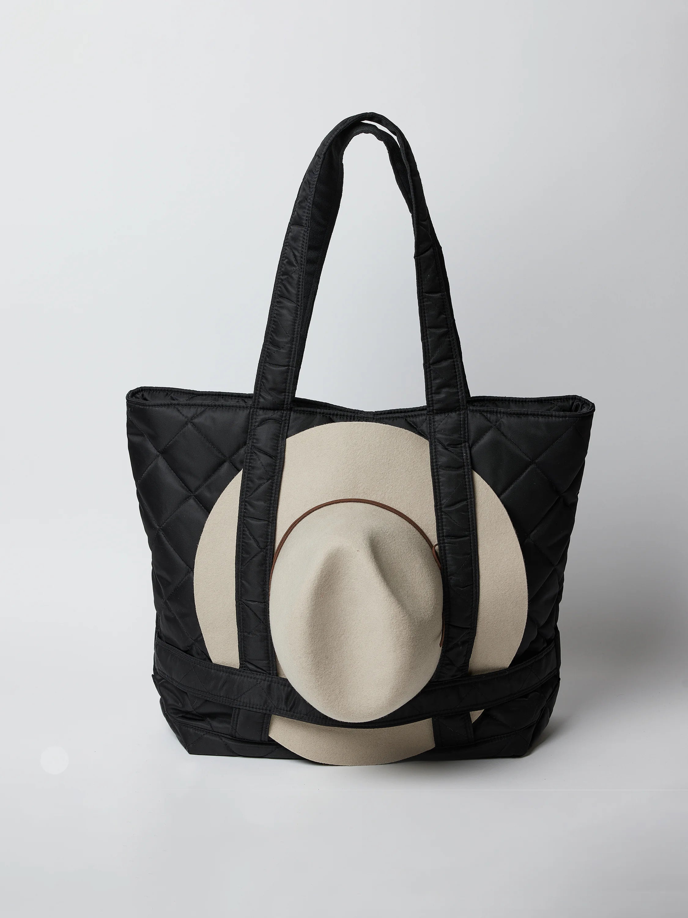 Black quilted tote bag with beige hat inside. Bag has black straps.