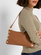 Saddle brown pebbled leather shoulder bag with gold studs on front, gold hardware, and red lining.