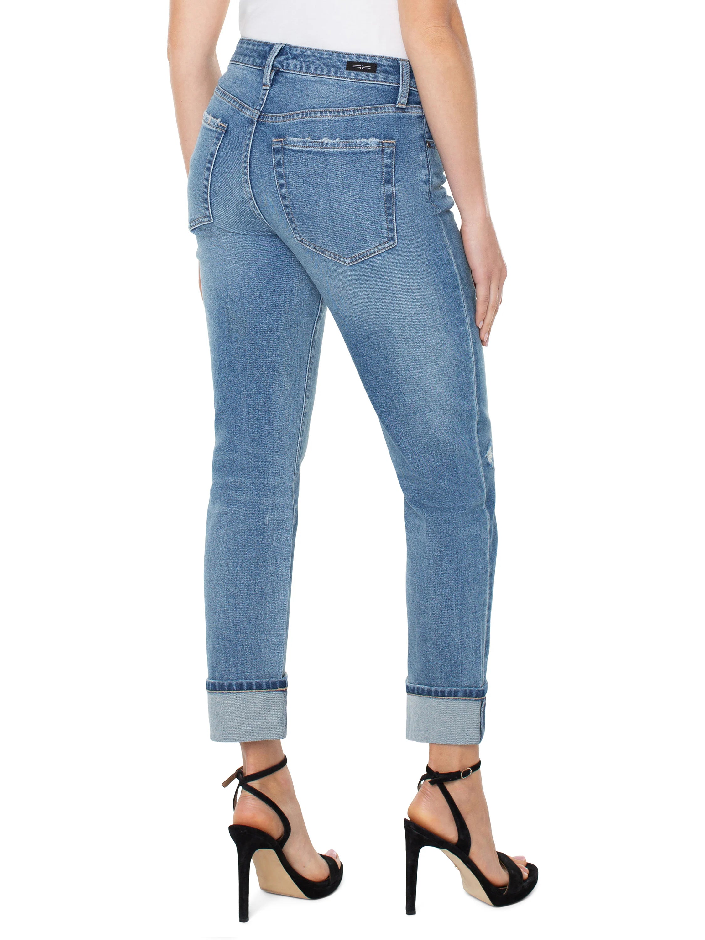 Light-wash blue jeans, rolled cuffs, slight distressing. Back view. Model also wearing black high heels.