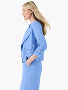 Blue linen moto jacket with draped lapels, two silver-buttoned flap pockets, and 3/4 sleeves with button tabs.