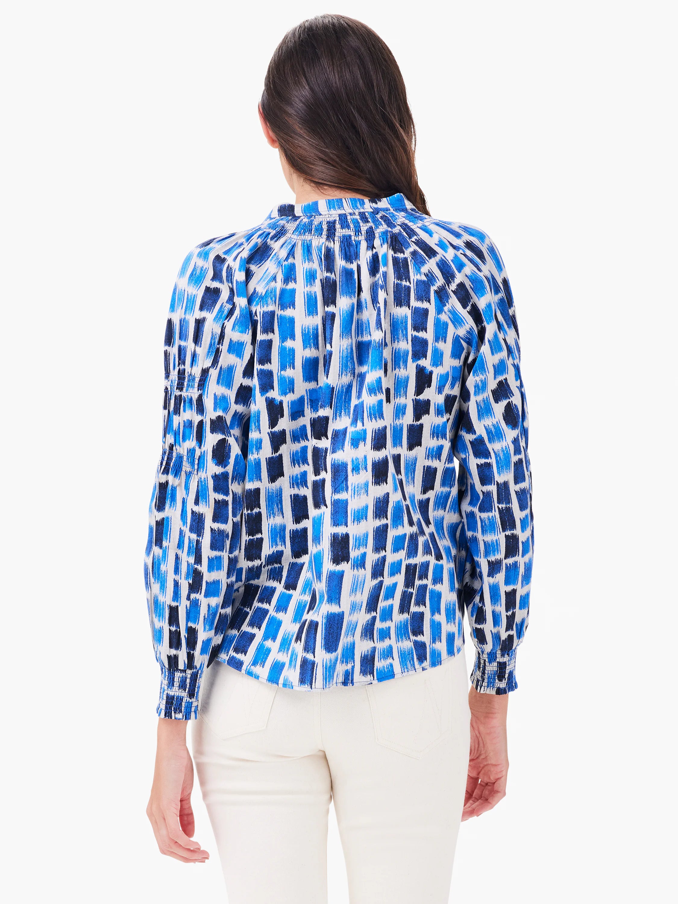 White long-sleeve top with varied blue brushstroke pattern. Gathered neck & smocked cuffs. Model's back view.