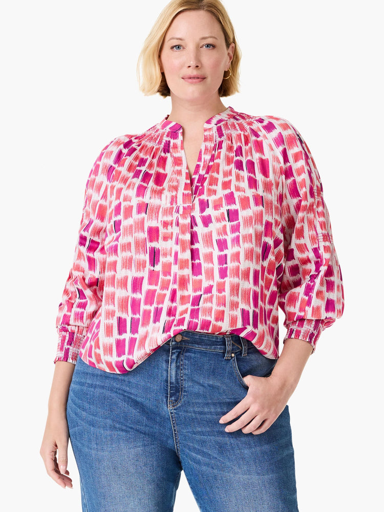 White top with abstract pink and fuchsia brushstrokes. Features V-neck, gathered collar, and 3/4 smocked sleeves.