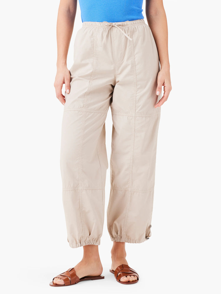 Beige ankle-length pants with drawstring waist and cuffed hems. Features stitched panels. Model wears brown sandals.
