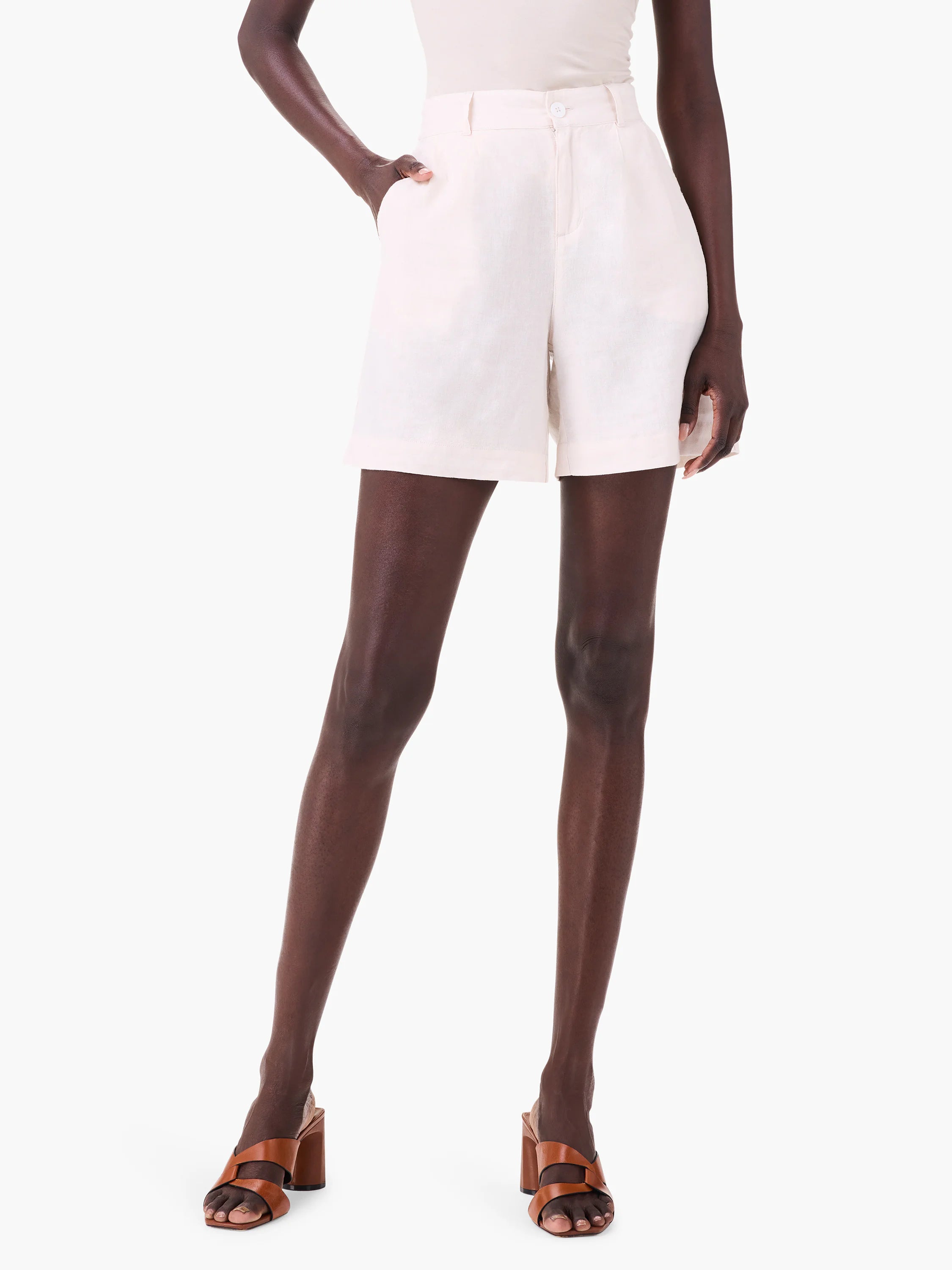 Off-white linen shorts on a model. The shorts have a high waist and pleated front. Model wears brown heels.