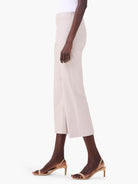 Pale beige wide-leg crop pants, shown on a model from the side, featuring a smooth, polished fabric.