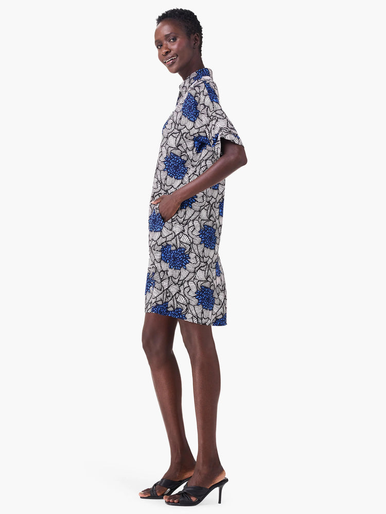 Off-white short-sleeved dress with a blue floral print. Black outlines on the flowers. The dress has pockets.