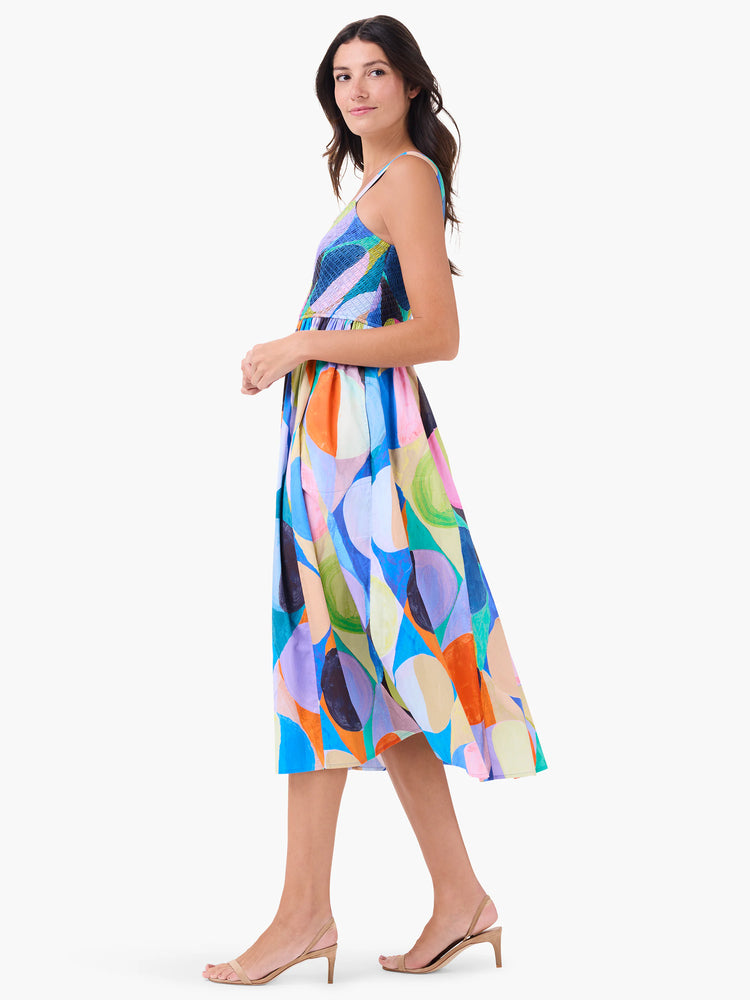 Midi dress, sleeveless, with an abstract print in blues, pinks, oranges, and greens. The skirt is pleated.