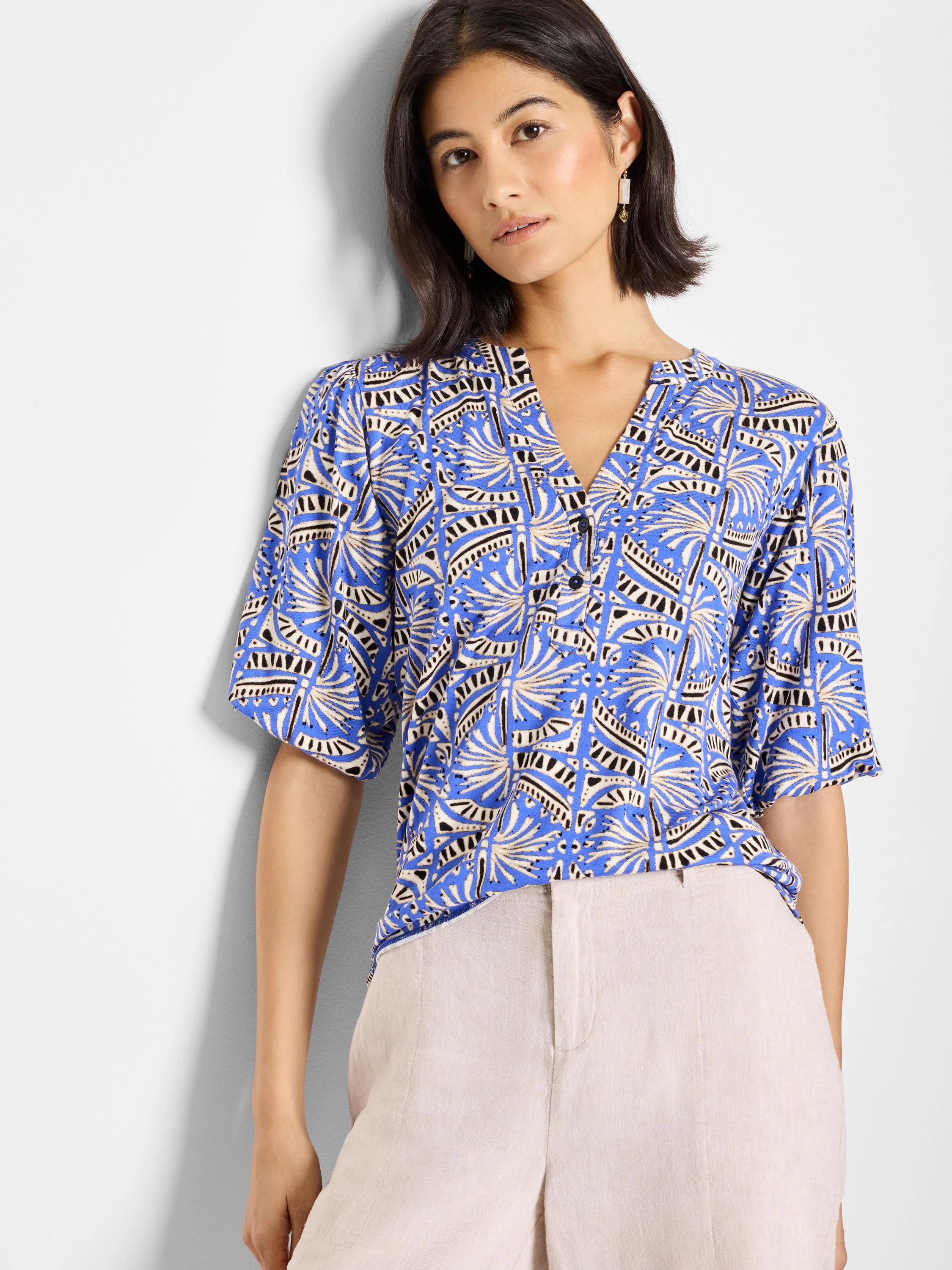 Blue top with a V-neck and short sleeves. Features a repeating geometric pattern in off-white and black.