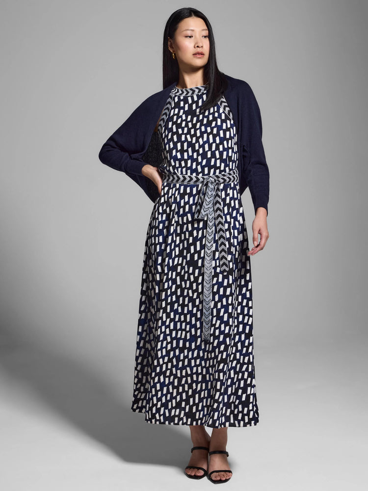 Navy blue shrug cardigan over a midi dress with a white and navy abstract print. Dress has a self-tie belt.