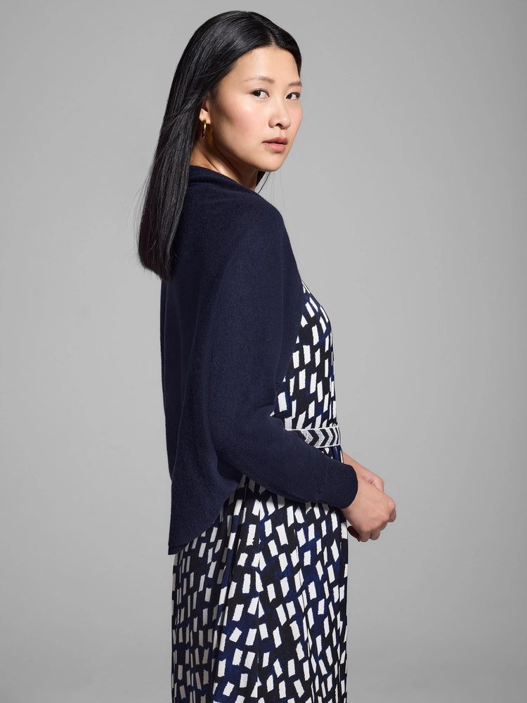 Navy blue shrug cardigan; three-quarter sleeves. Shown over a white and navy blue patterned dress.