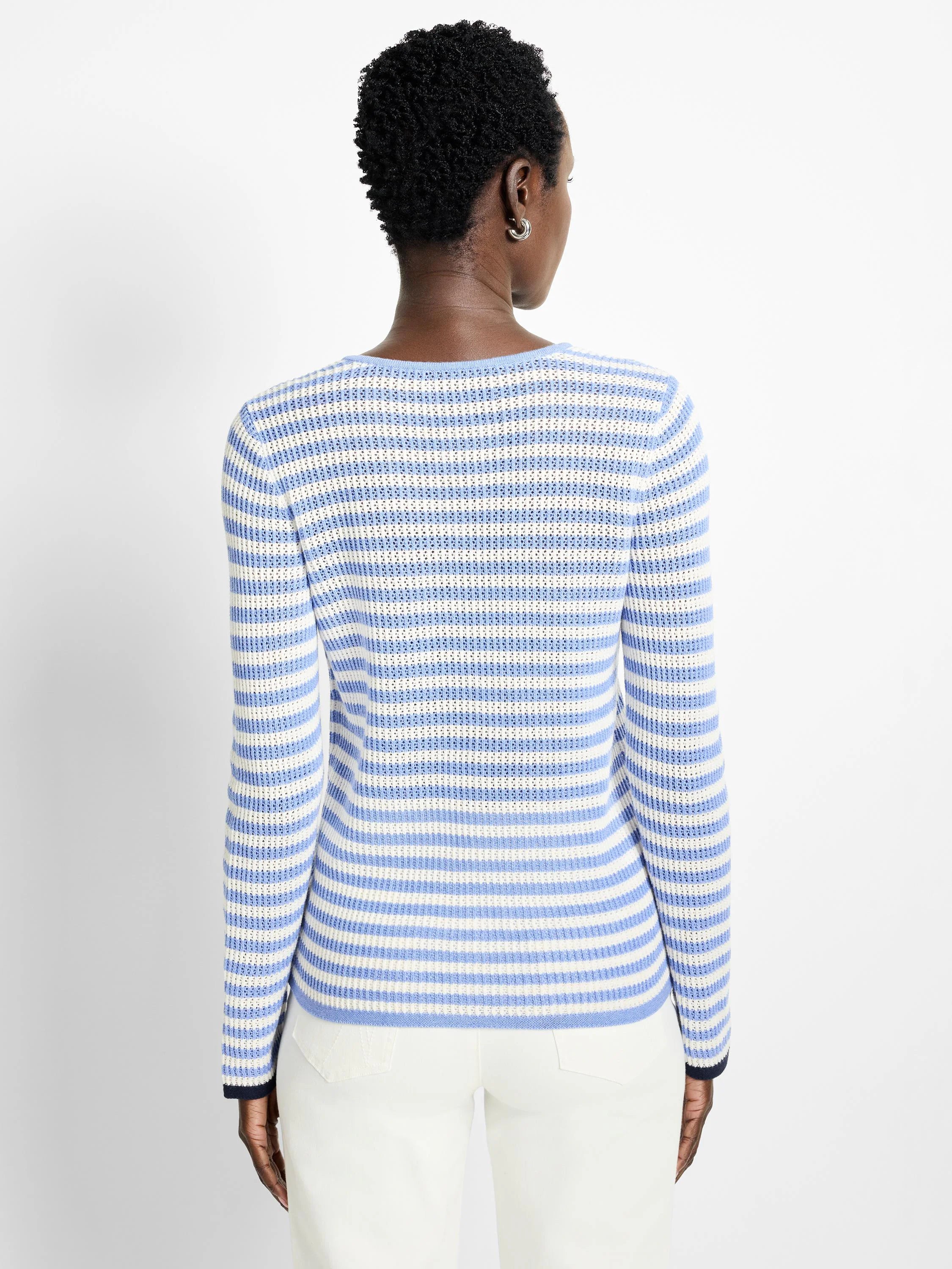 Back view of light blue and white horizontally striped, long-sleeved mesh sweater. Navy blue cuffs.