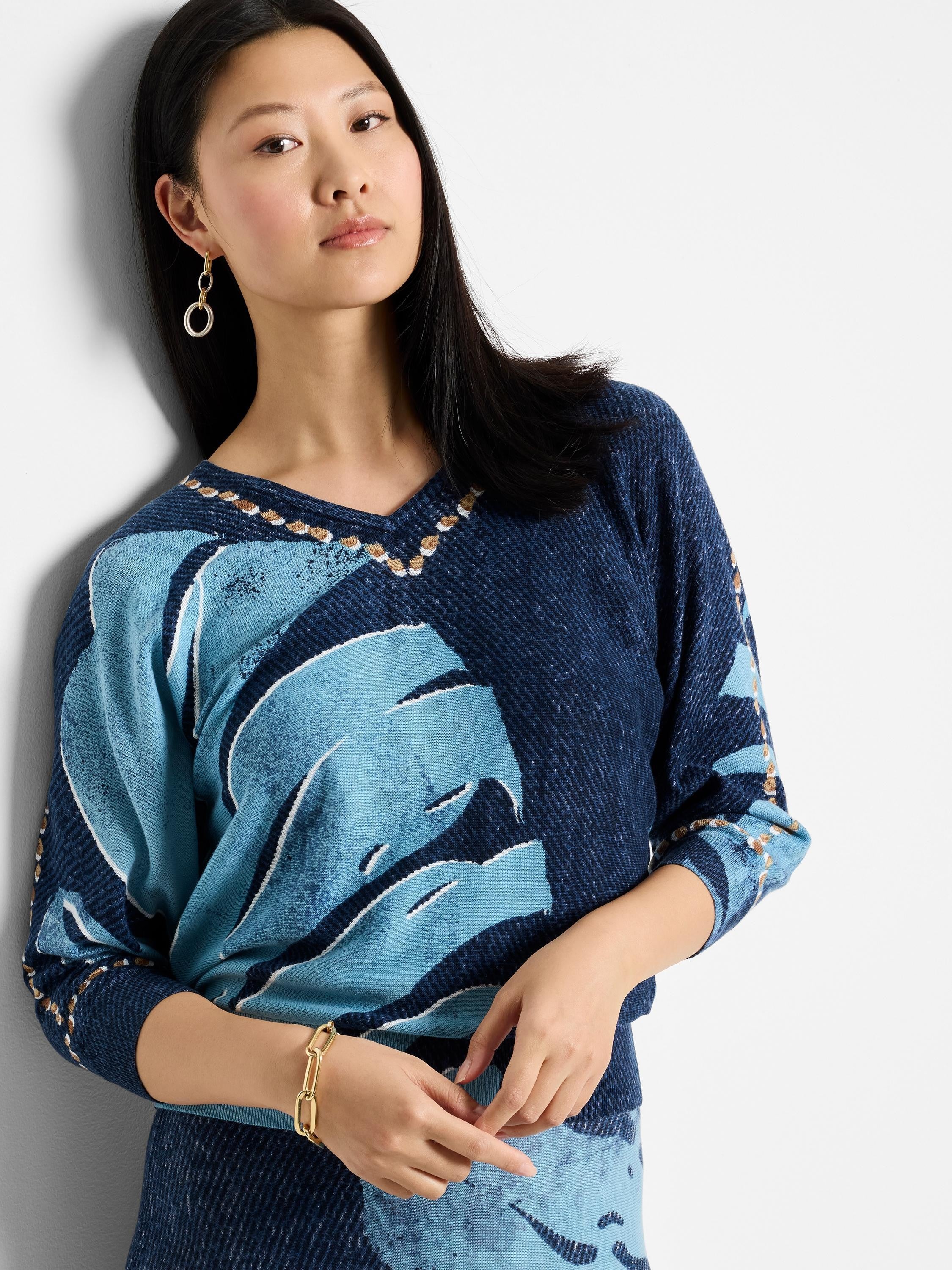 V-neck sweater; navy blue and light blue abstract leaf pattern; brown and gold neckline detail. Three-quarter sleeves.