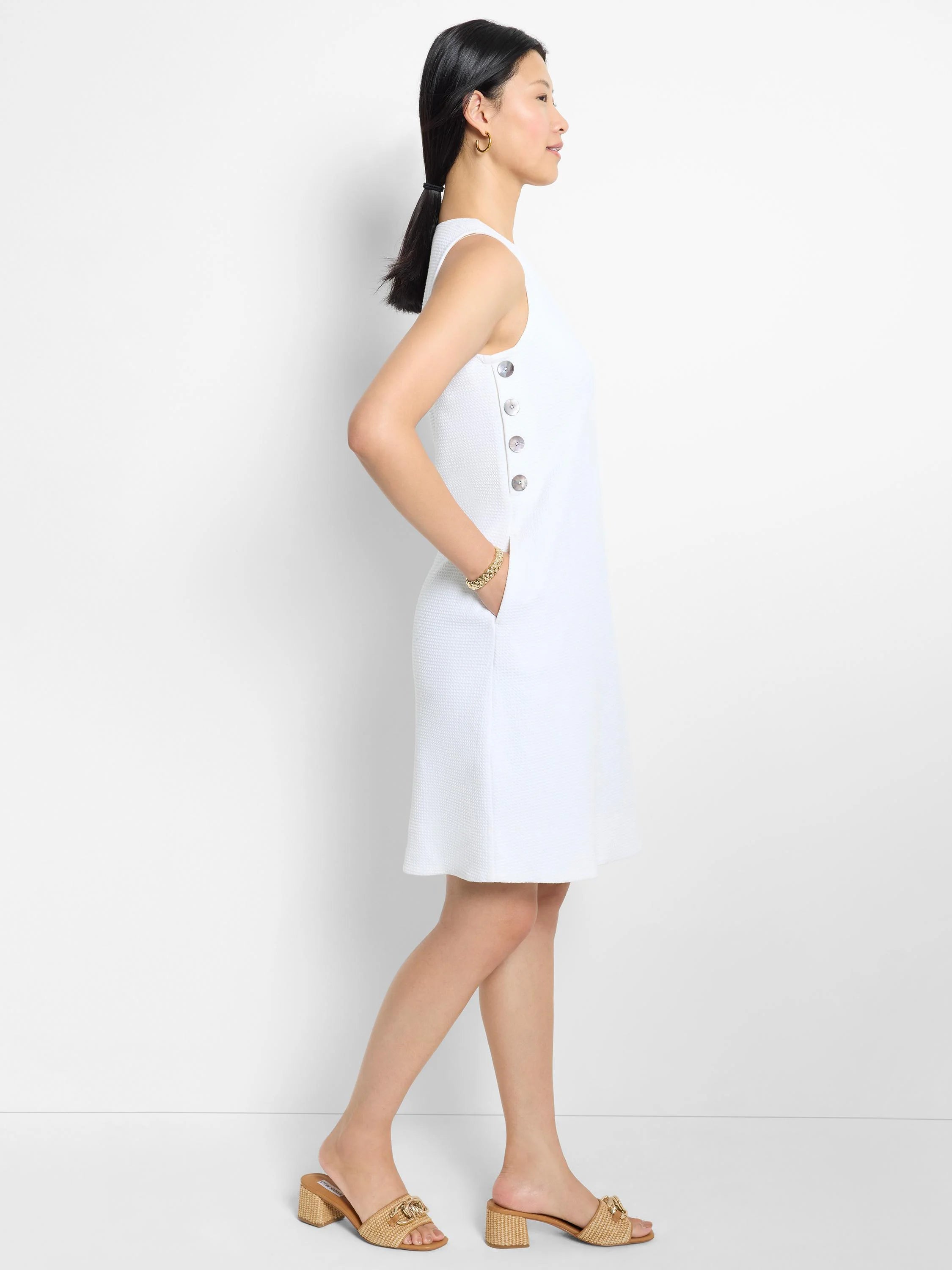 White textured sleeveless mini dress with a row of buttons on the side. Features pockets.