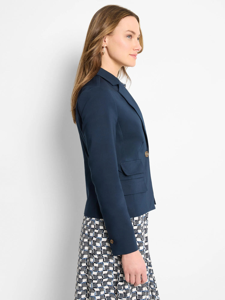 Navy blue blazer, single button, two pockets. Model shown wearing it with a black and white patterned dress.