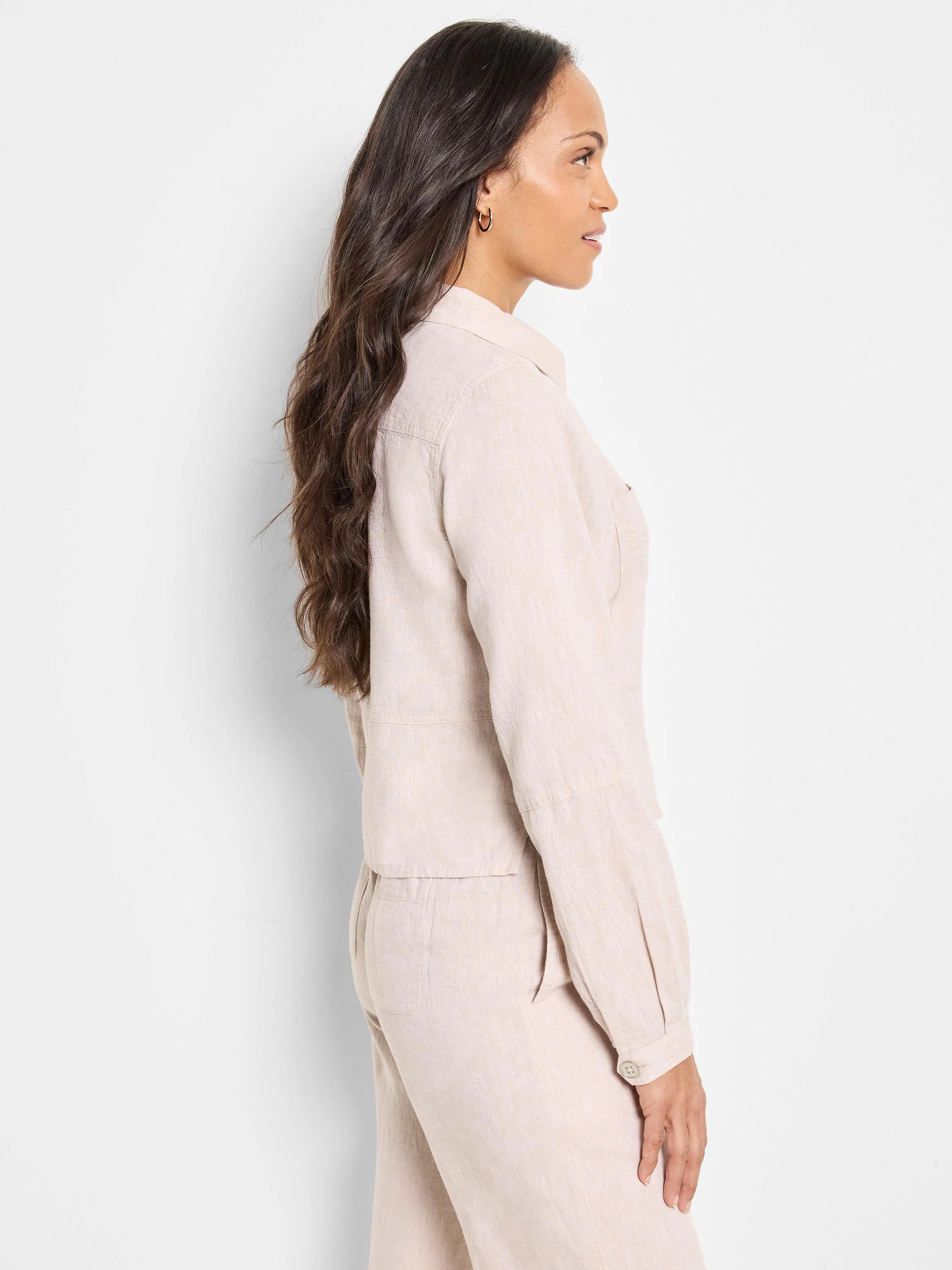 Beige linen jacket, shown from the side. Long sleeves, button cuffs, and pockets. Linen texture visible.