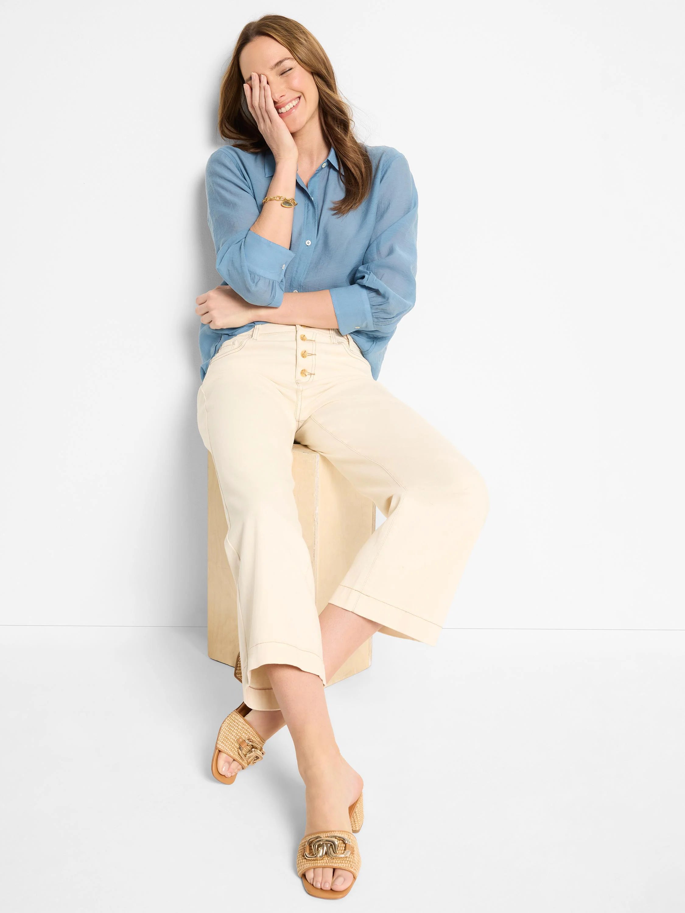 Light blue, long-sleeve button-down shirt. Model is smiling and wearing off-white pants.